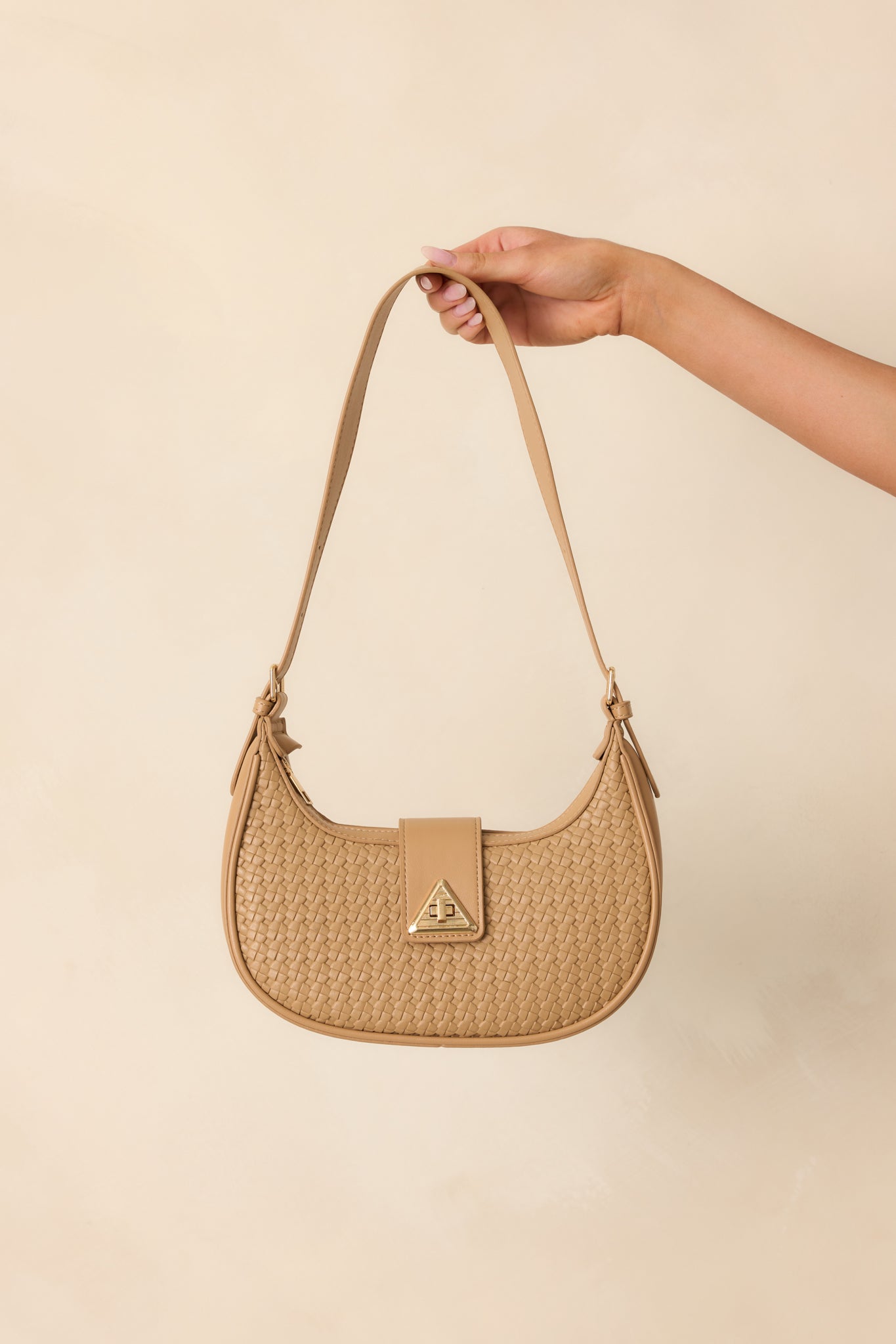 Front-facing full view of the beige shoulder bag showing the curved half-moon silhouette, woven faux leather texture, and gold triangular twist-lock flap closure.
