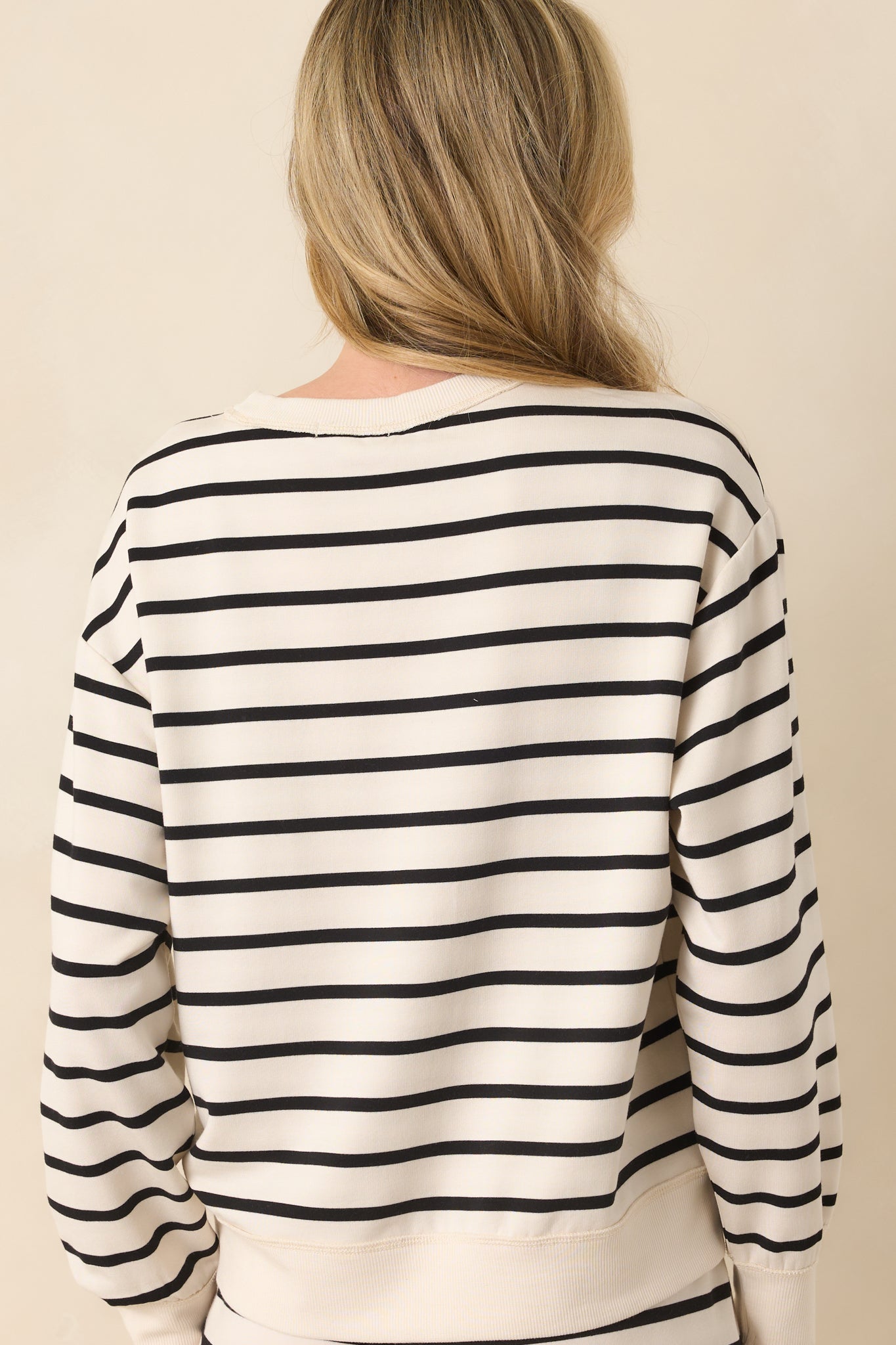 A back view of the sweatshirt displaying the continuation of the light beige and black stripes and relaxed shape across the shoulders.
