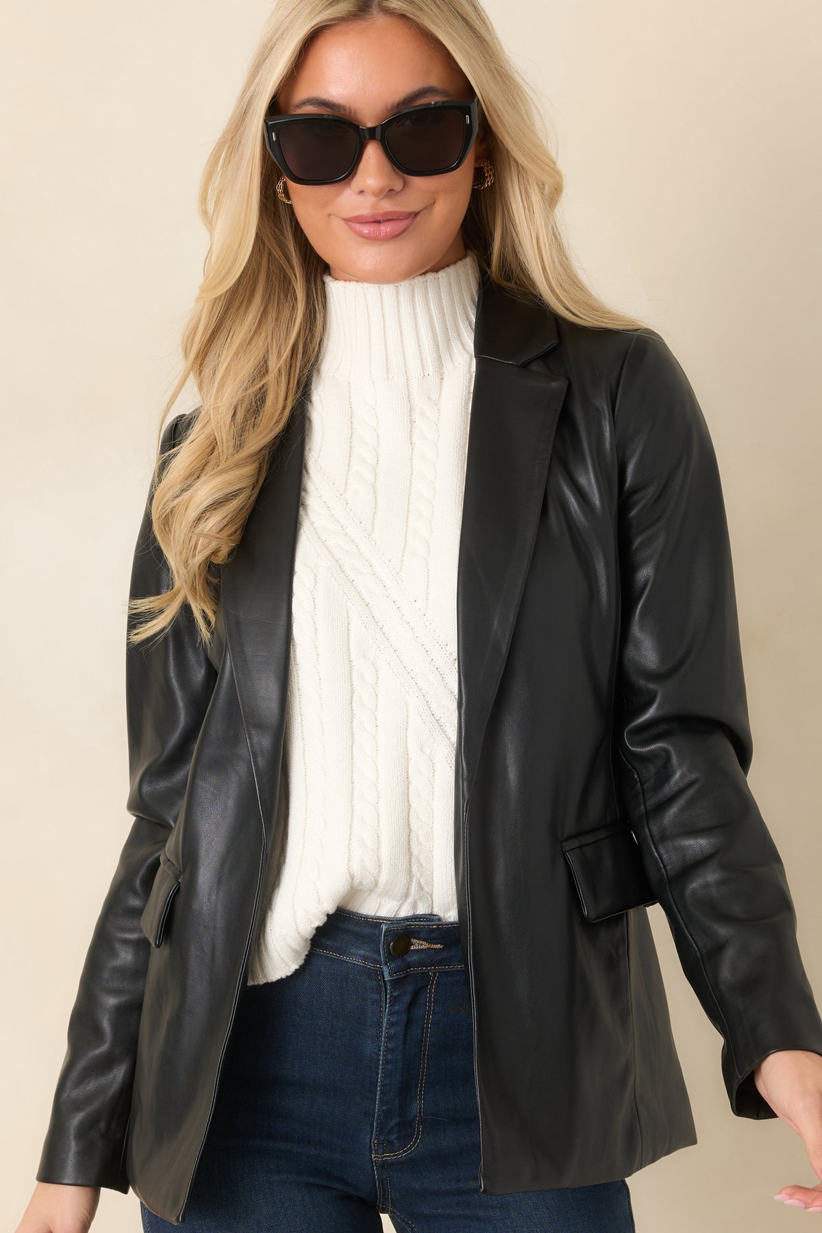 Curved stitching shapes the waist of the black faux leather blazer beneath its structured lapels.