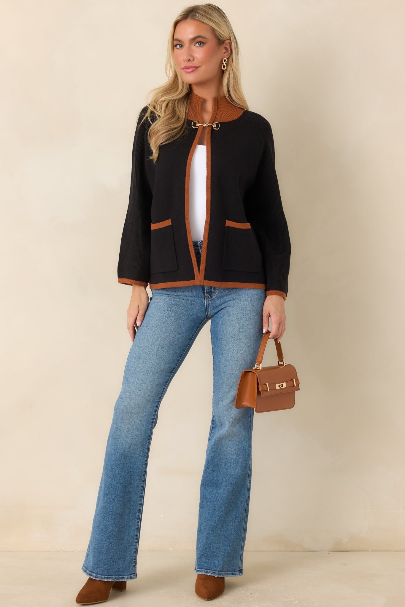 Black knit cardigan featuring warm brown contrast trim, a relaxed open-front silhouette, ribbed edges, patch pockets, and a polished gold-tone horsebit closure.