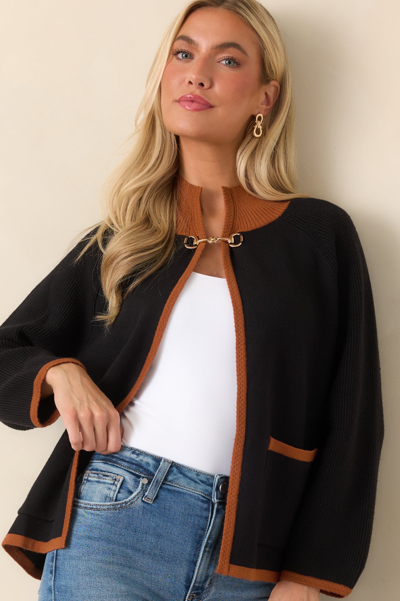 Cropped view of the black knit cardigan featuring warm brown trim along the cuffs and hem, emphasizing its polished color-blocked design.