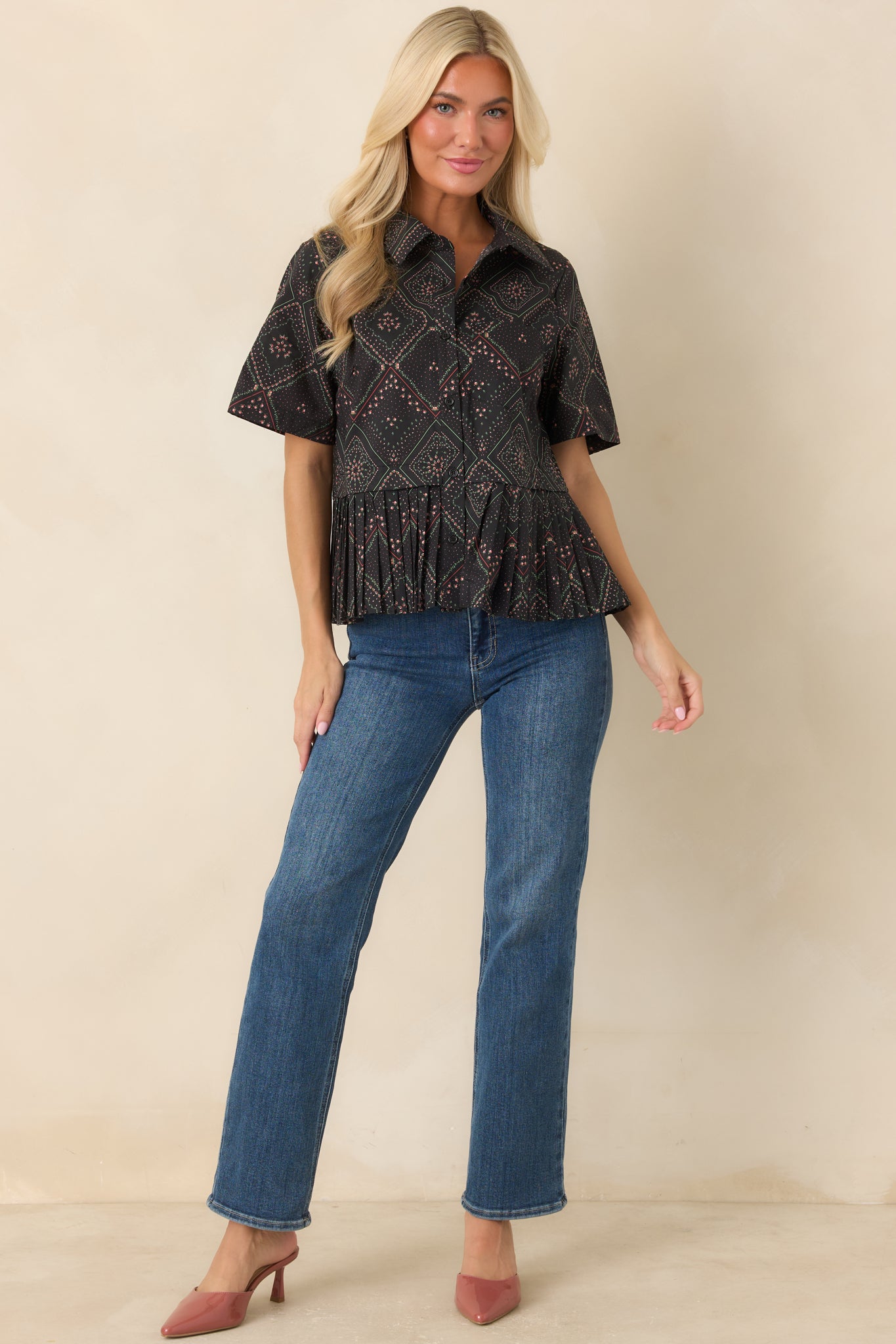Black 100% cotton blouse featuring a scarf-inspired geometric print with coral and green floral motifs, a collared neckline, functional button-front closure, short sleeves, and a sharply pleated peplum hem.