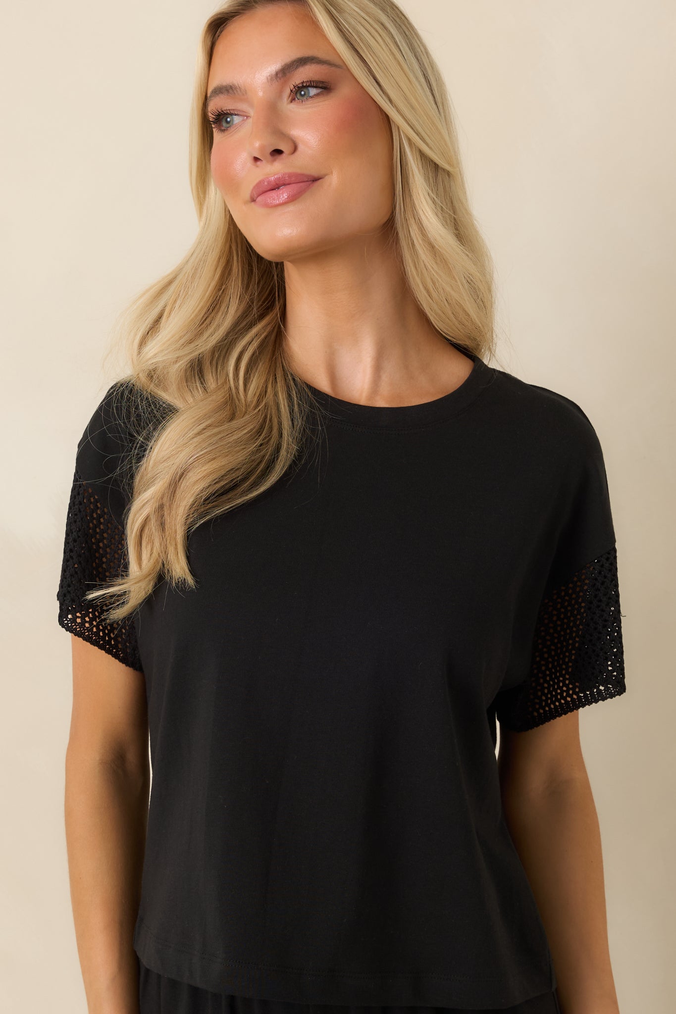Black top featuring a clean crew neckline, easy cropped length, and decorative crochet trim along the short sleeves.
