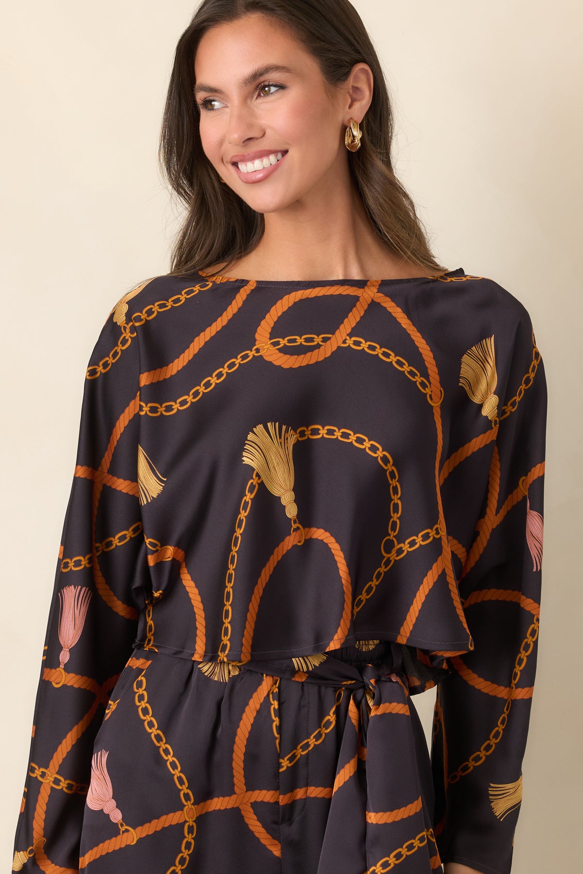 Black satin-feel top showcasing its relaxed cropped cut and contrasting rust, gold, and tassel print.