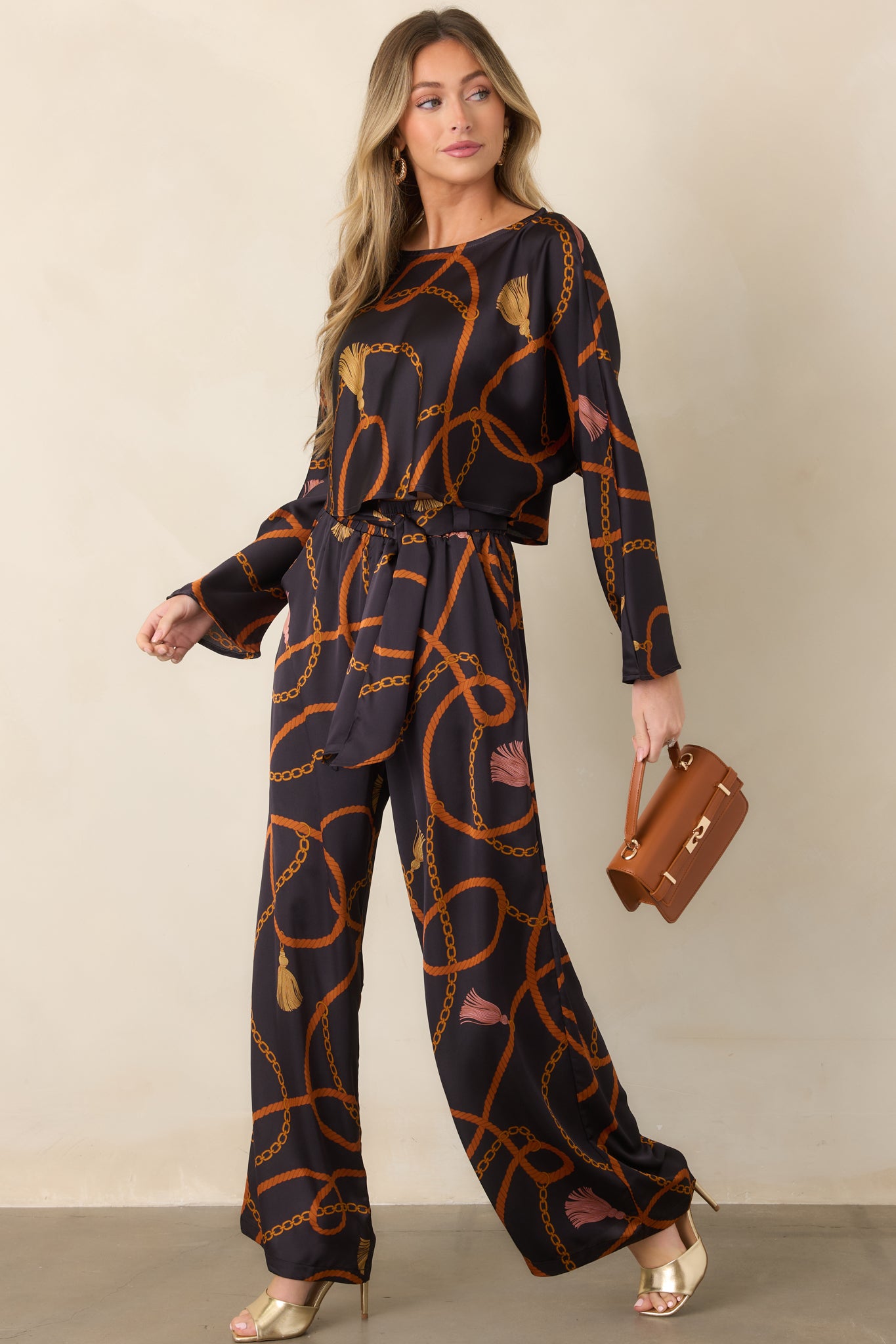 Cropped black top featuring a fluid drape and decorative rust, gold, and tassel-inspired print.
