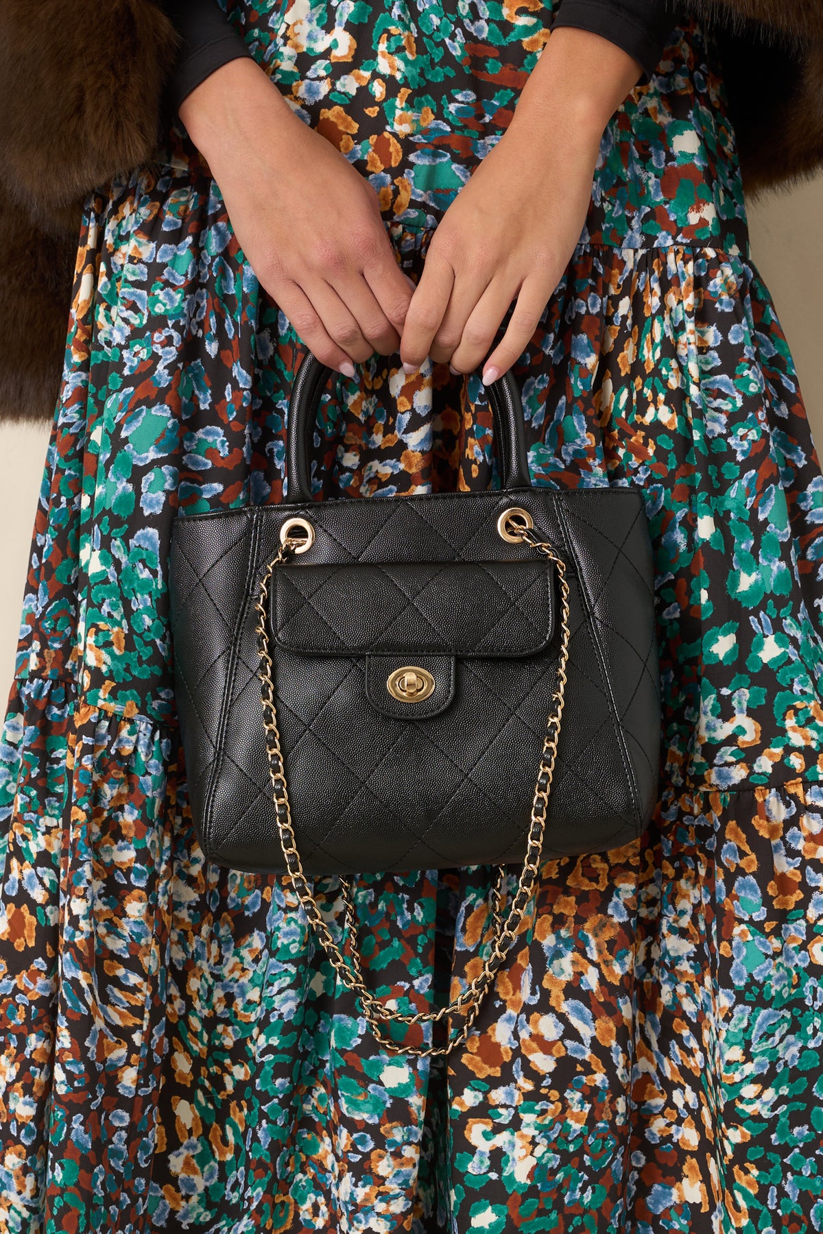 Black diamond-quilted handbag with gold-tone hardware, top handles, and chain-accented shoulder straps.