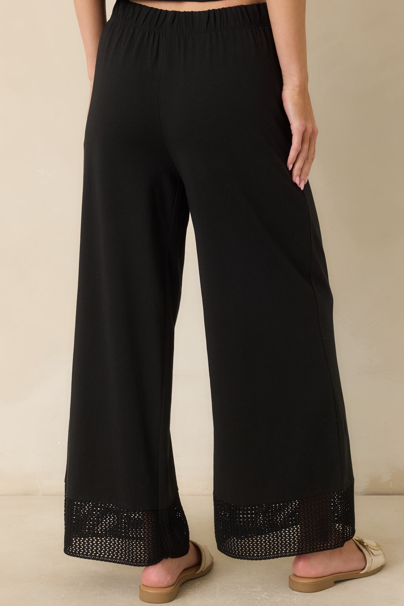 Rear view of the black cotton and lyocell jersey pants featuring a relaxed straight-leg fit, elastic waistband, and crochet lace hem.