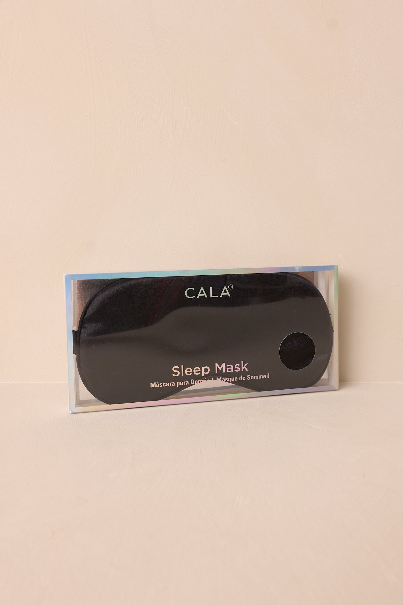 The black eye mask displayed on a beige background, emphasizing its sleek satin material and elegant design.