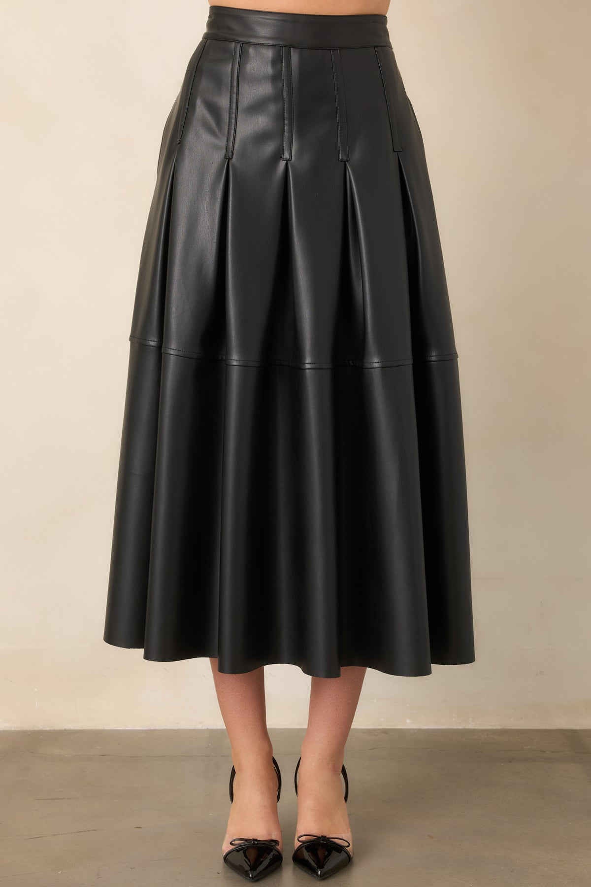 Black faux leather midi skirt showcasing the smooth waistband and neatly defined vertical pleating.