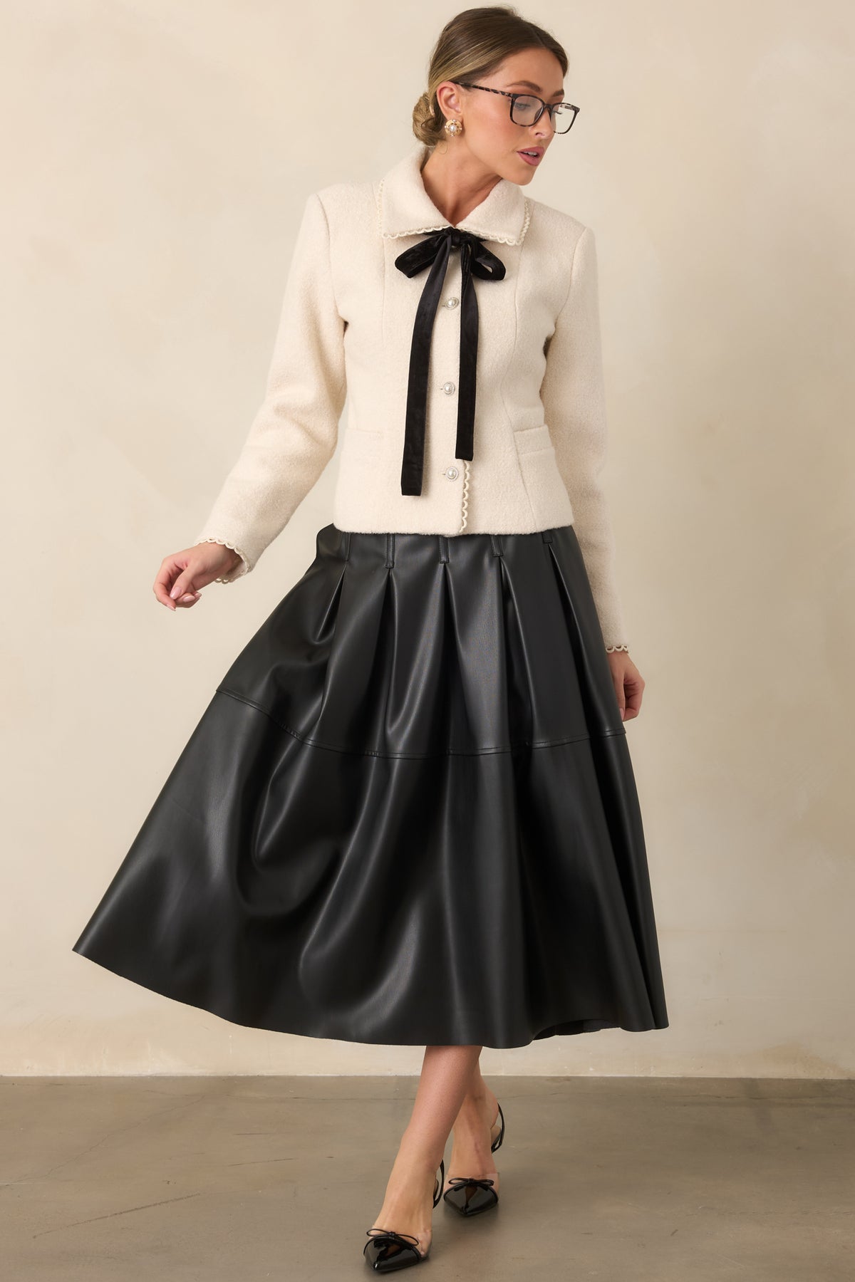 Black faux leather skirt highlighting the structured pleats through the fitted waist and upper silhouette.