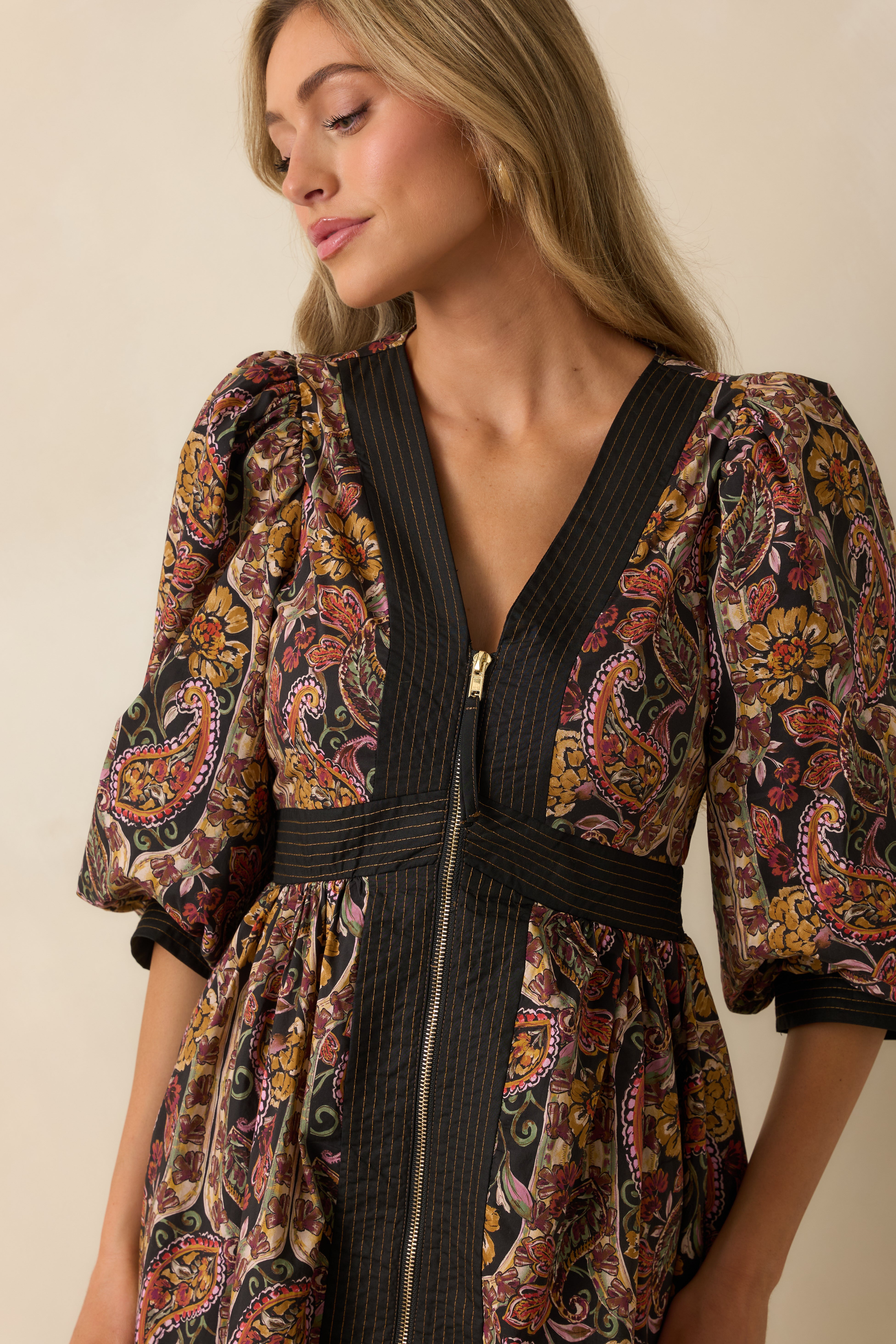 Close-up of the deep V-neckline, striped waist detailing, and puff sleeve design on the black floral dress.