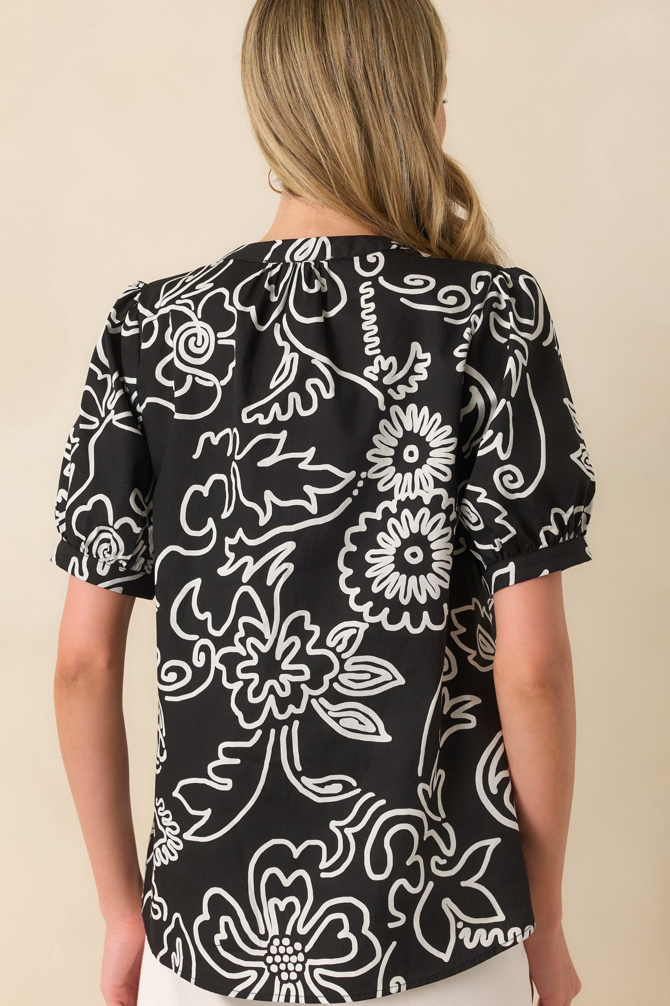 The back view of the black top displaying the continuous floral print and relaxed cut across the shoulders and back.