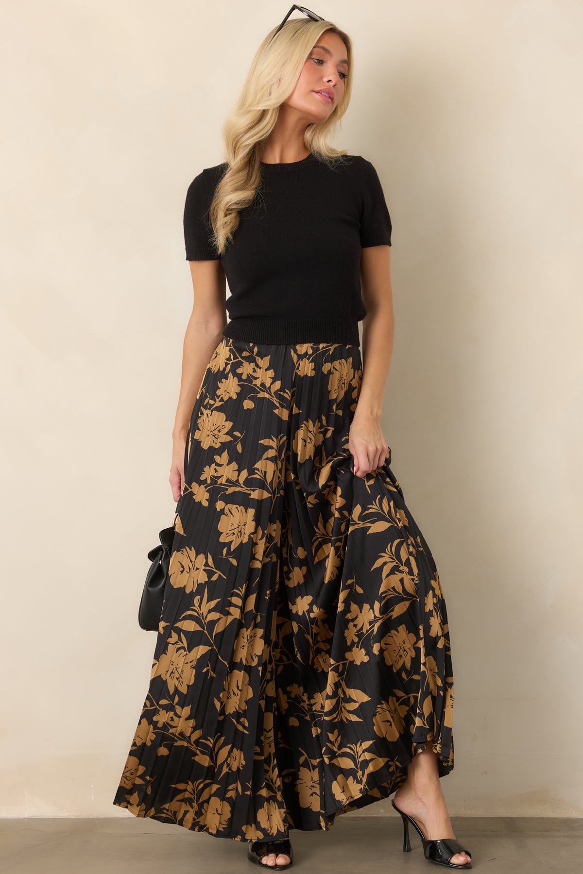 Black wide-leg pants covered in golden floral silhouettes with fine accordion pleats and a flowing shape.