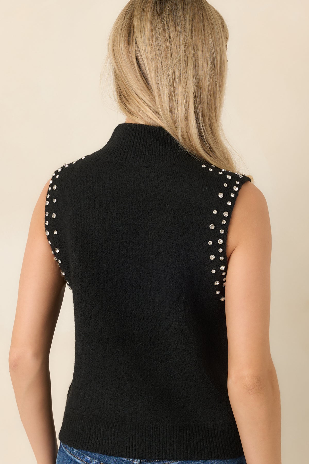 Back of the sleeveless black knit top featuring rhinestone accents along the edges and a ribbed mock neckline.
