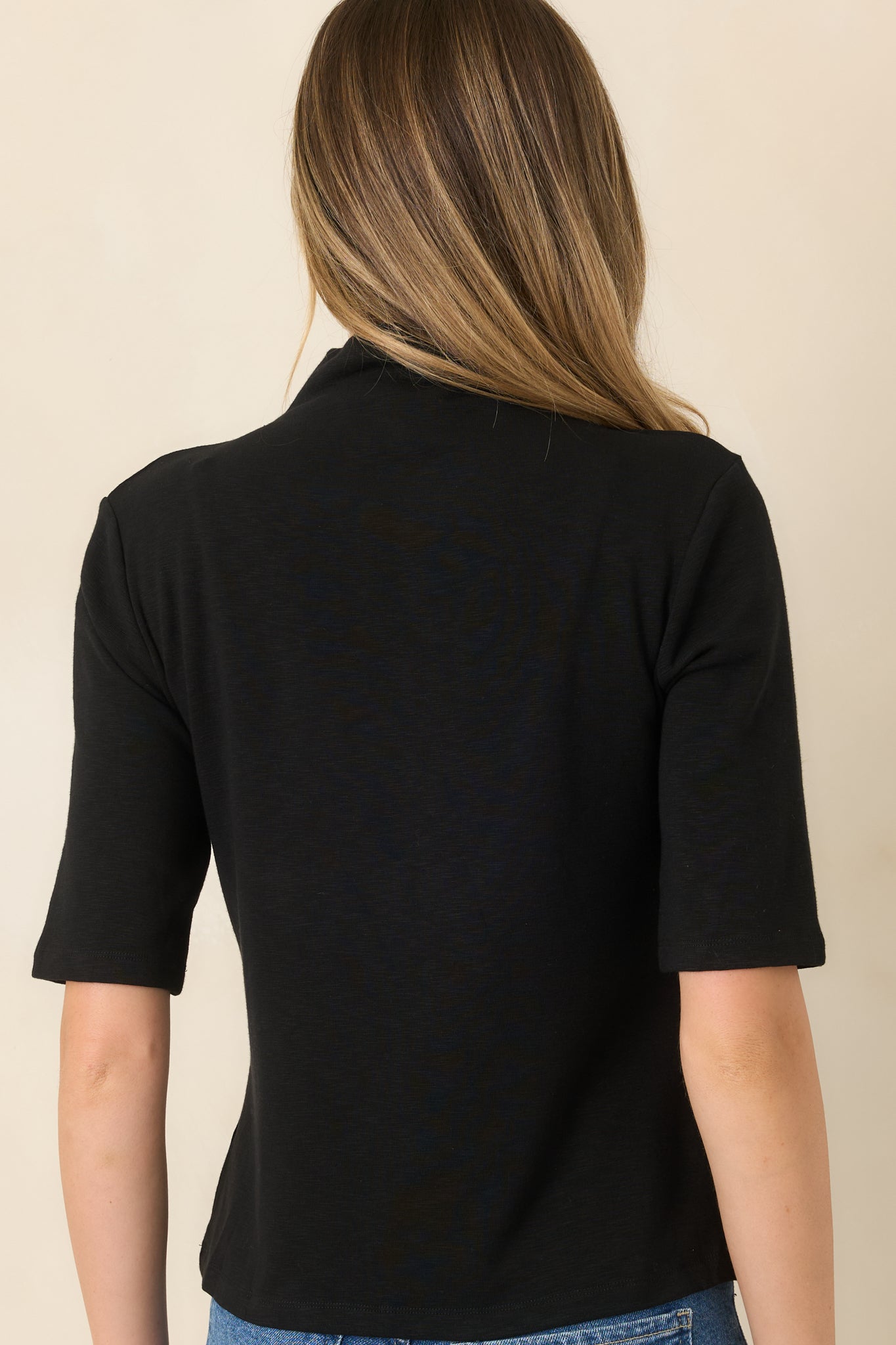 Rear view of the black knit top featuring a smooth back, gently fitted silhouette, and sleek stretch fabric construction.
