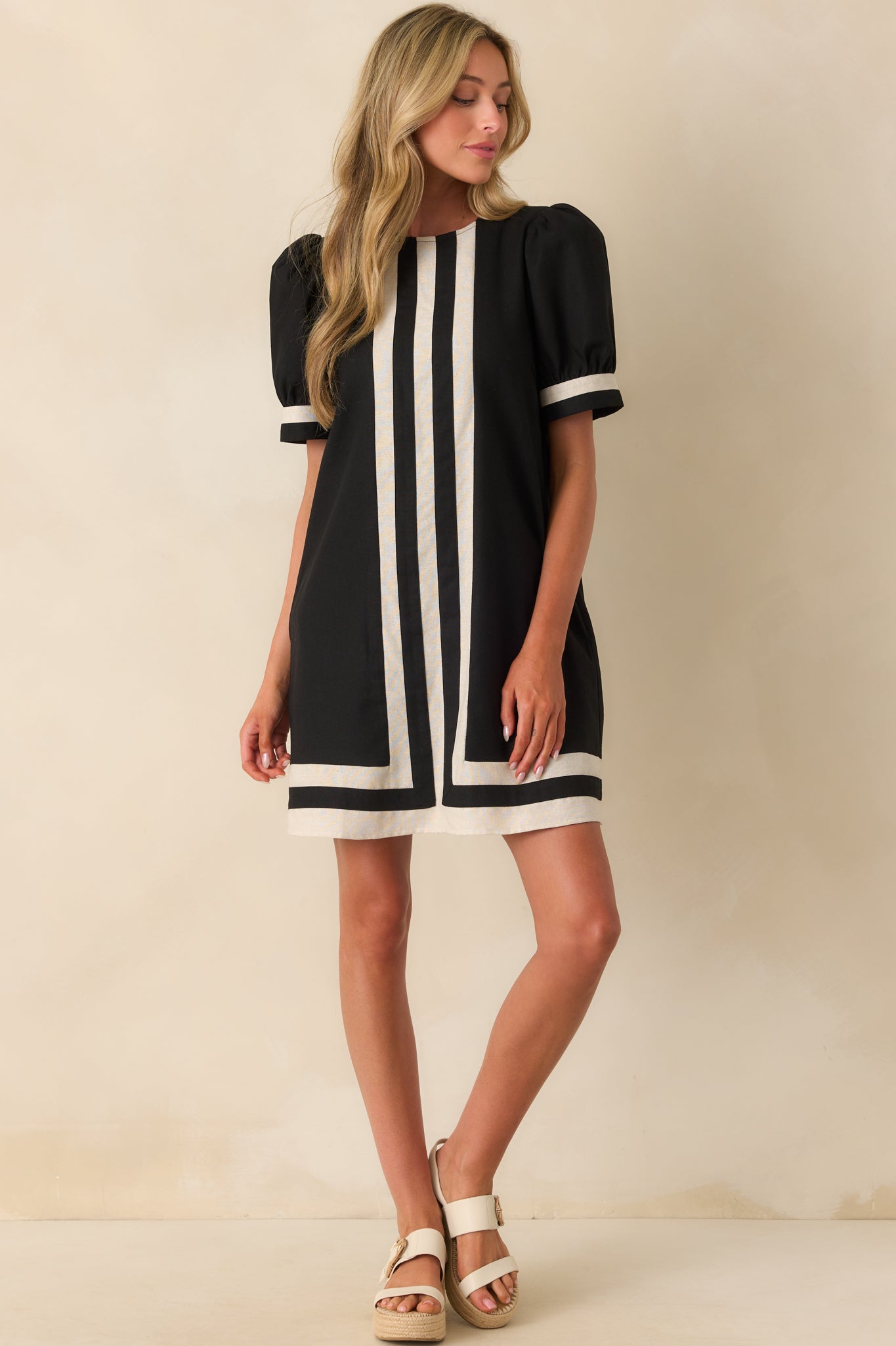 A full front view of the black mini dress showcasing the light beige contrast trim, center stripe detailing, and puff sleeves.