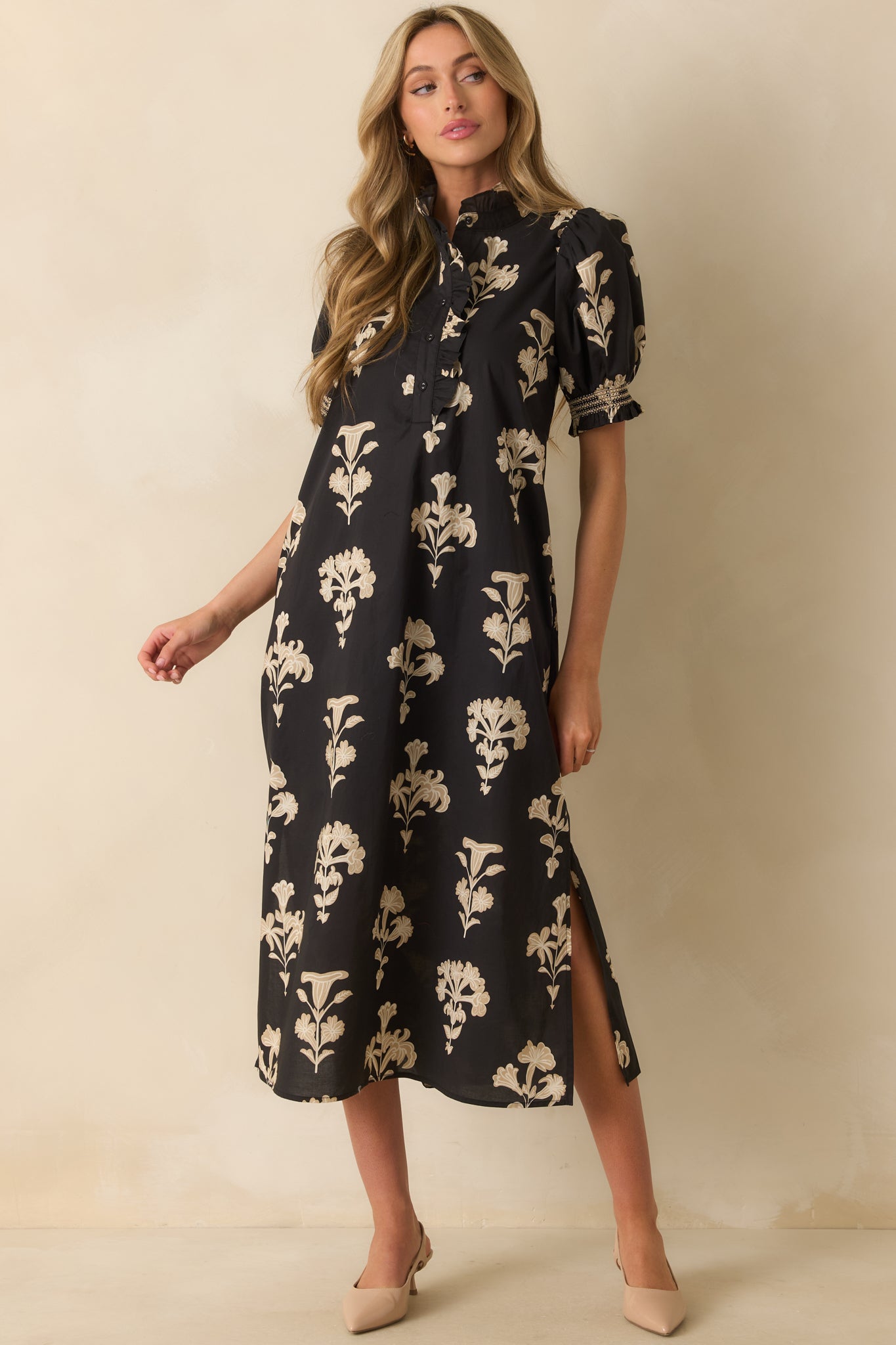 Black maxi dress with ivory floral print, ruffled mock neckline, short puff sleeves with smocked cuffs, and side slit hem for a flowing silhouette.