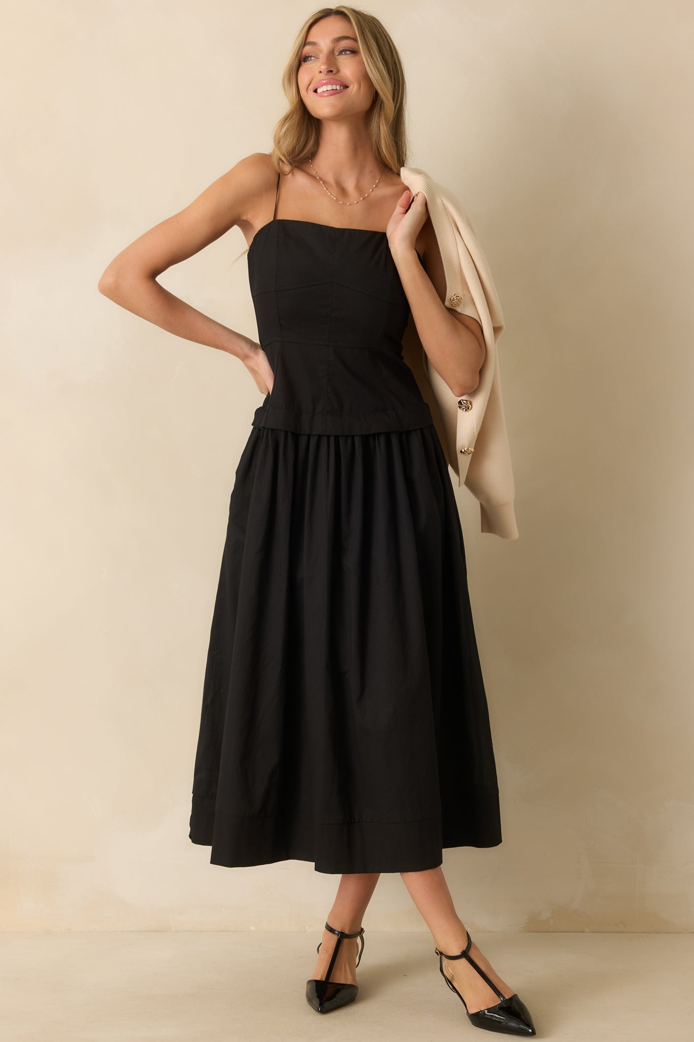 Black midi dress with bustier-style paneled bodice, adjustable spaghetti straps, and a gathered flowy skirt with functional pockets.