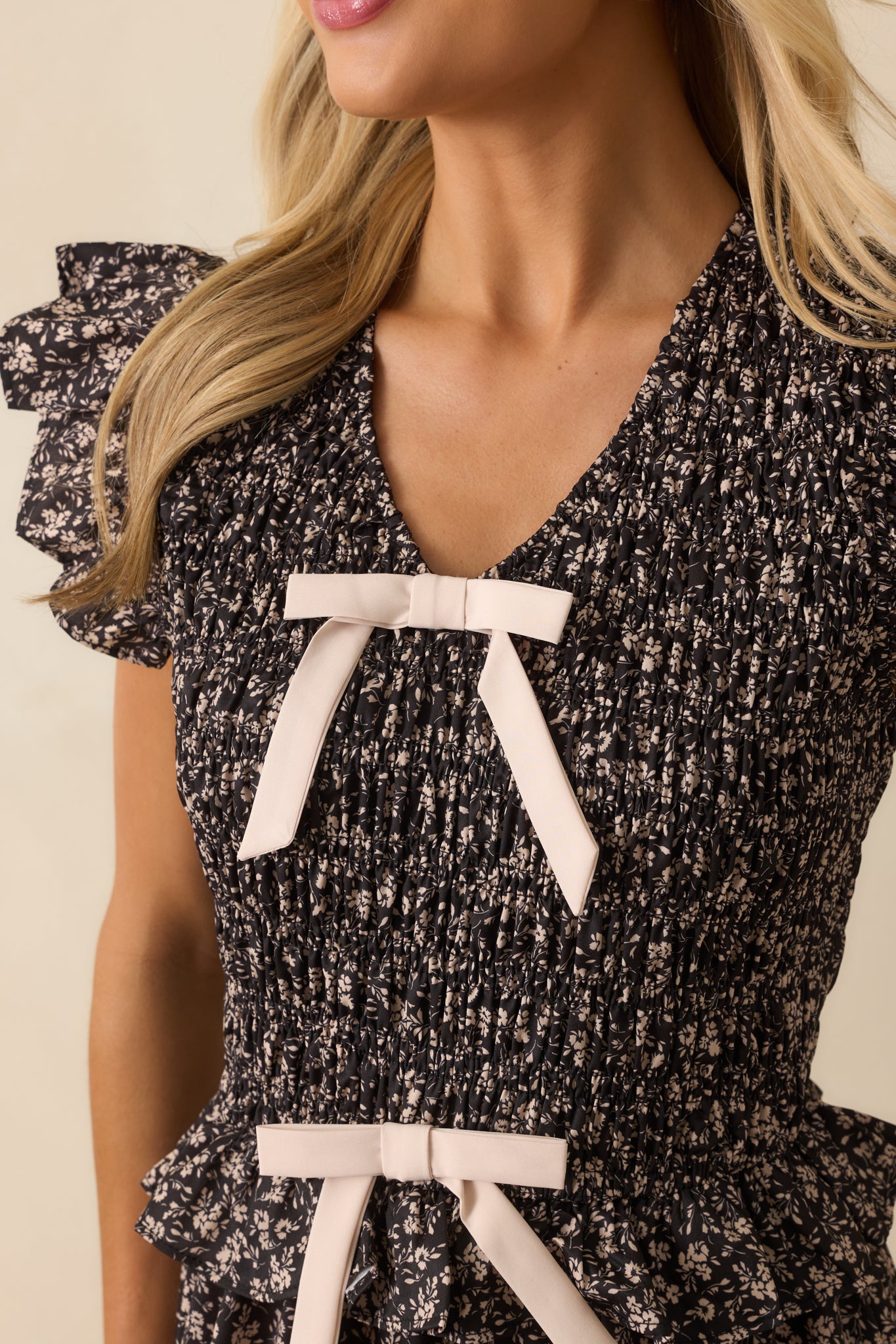 Close-up of the smocked bodice, ivory bow accents, and floral print on the black midi dress.