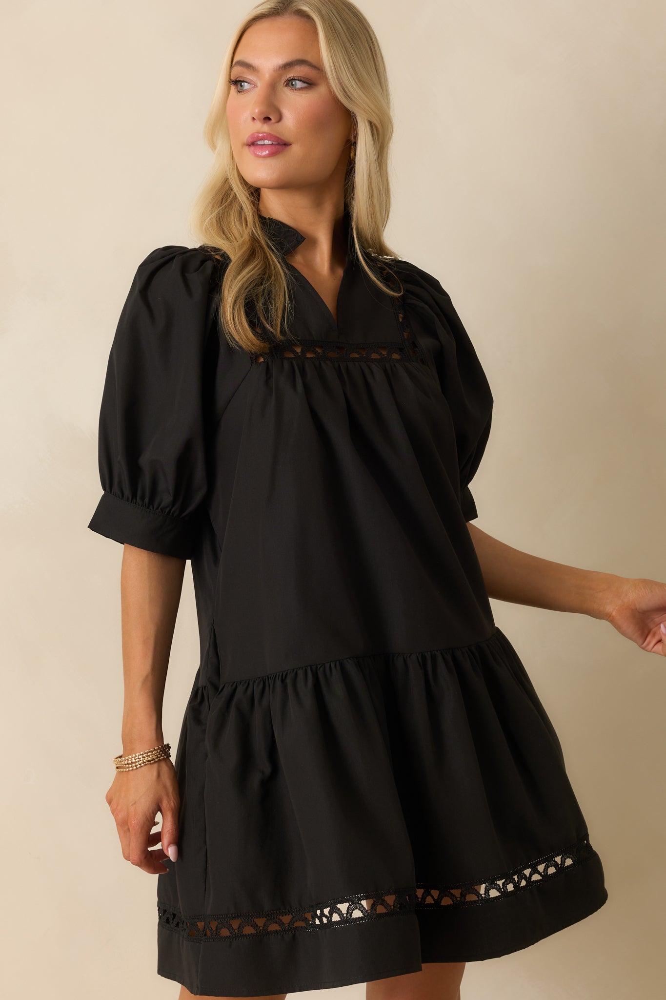 Detail of the black mini dress showing ruffle trim along the v-neckline, ladder lace panels, and puff sleeves.