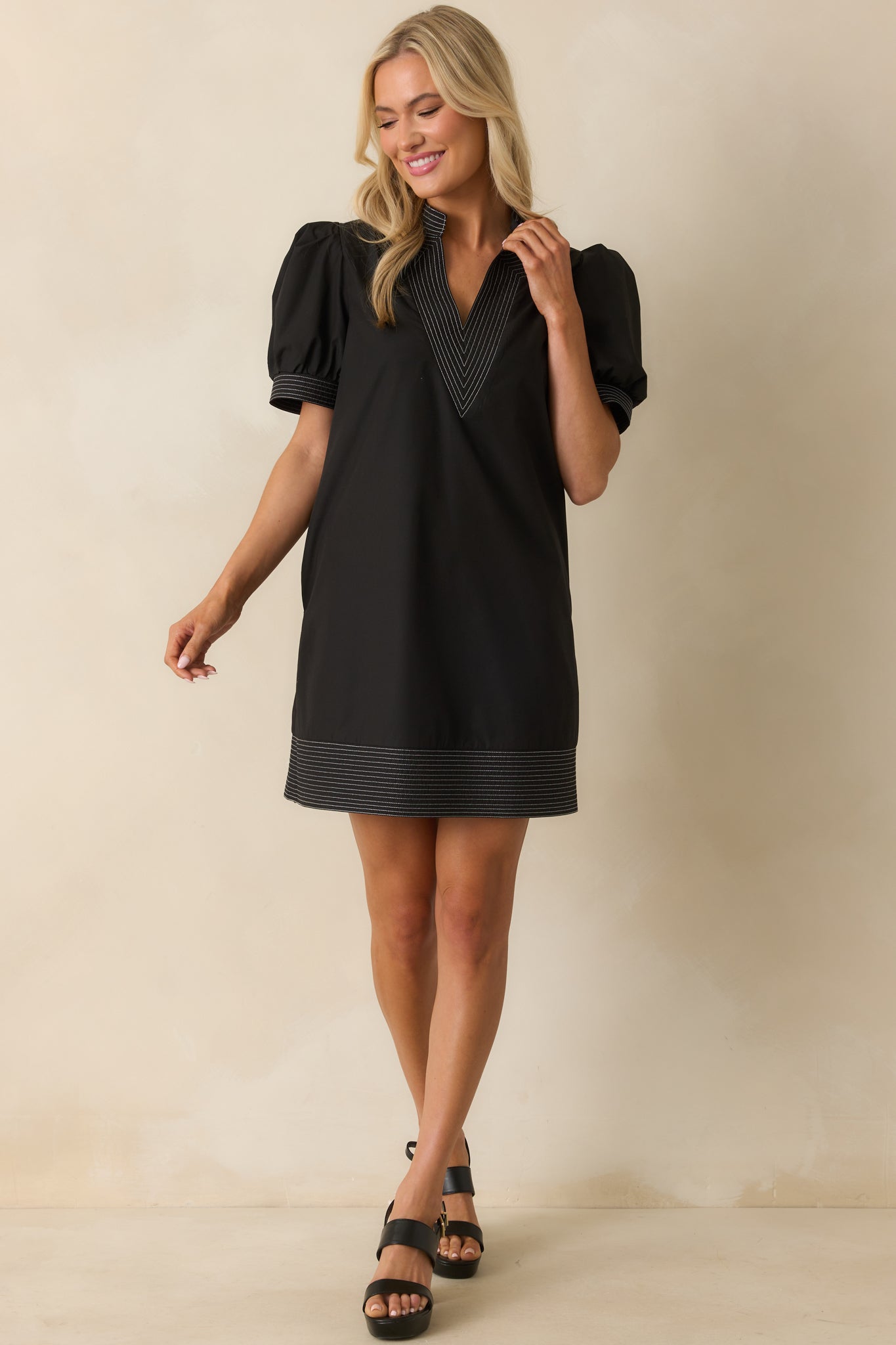 Black mini dress with a notch v-neckline and puff sleeves outlined by bold white topstitch trim.