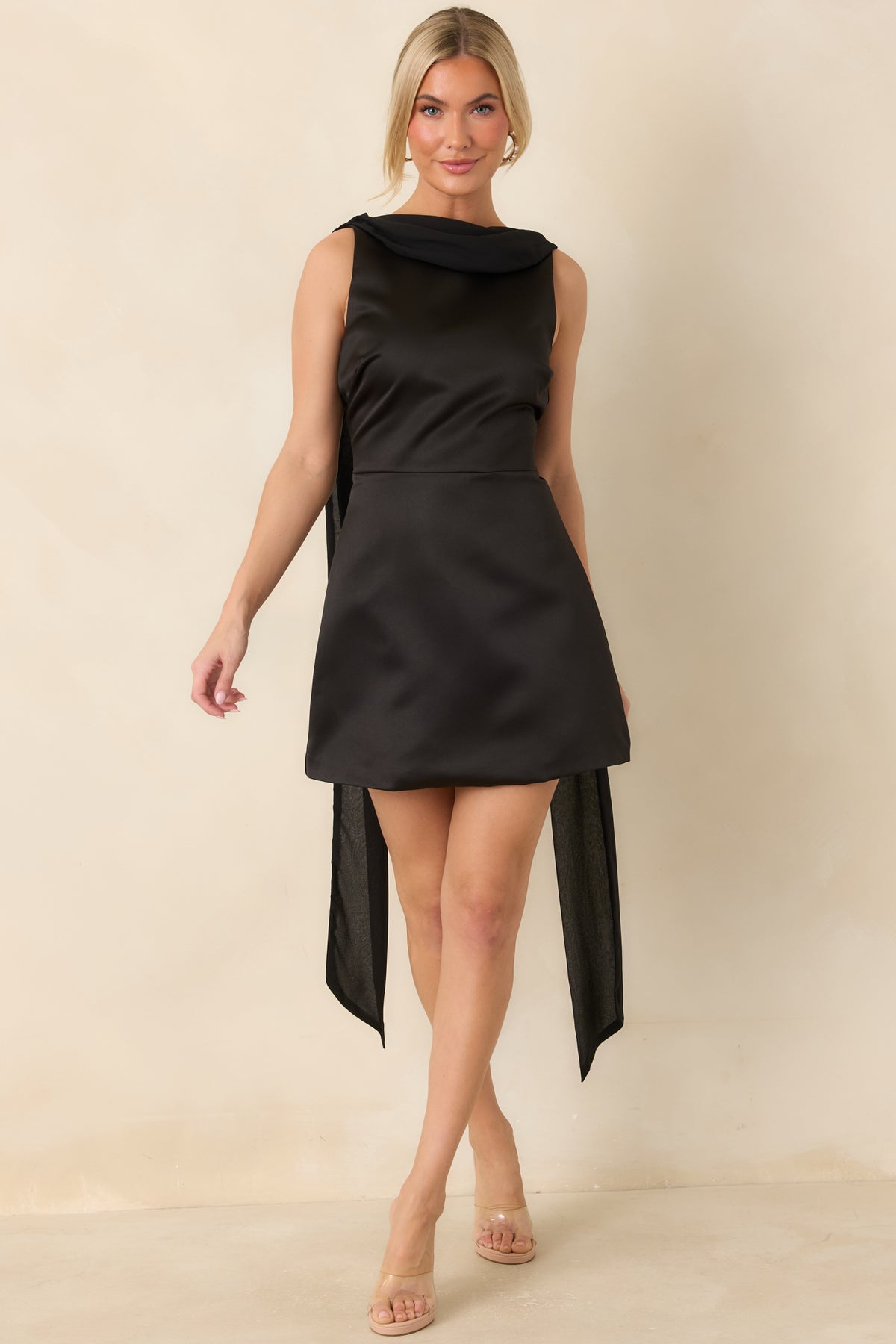 Elegant black mini dress with a smooth satin finish, defined waistline, and sheer shoulder scarf.