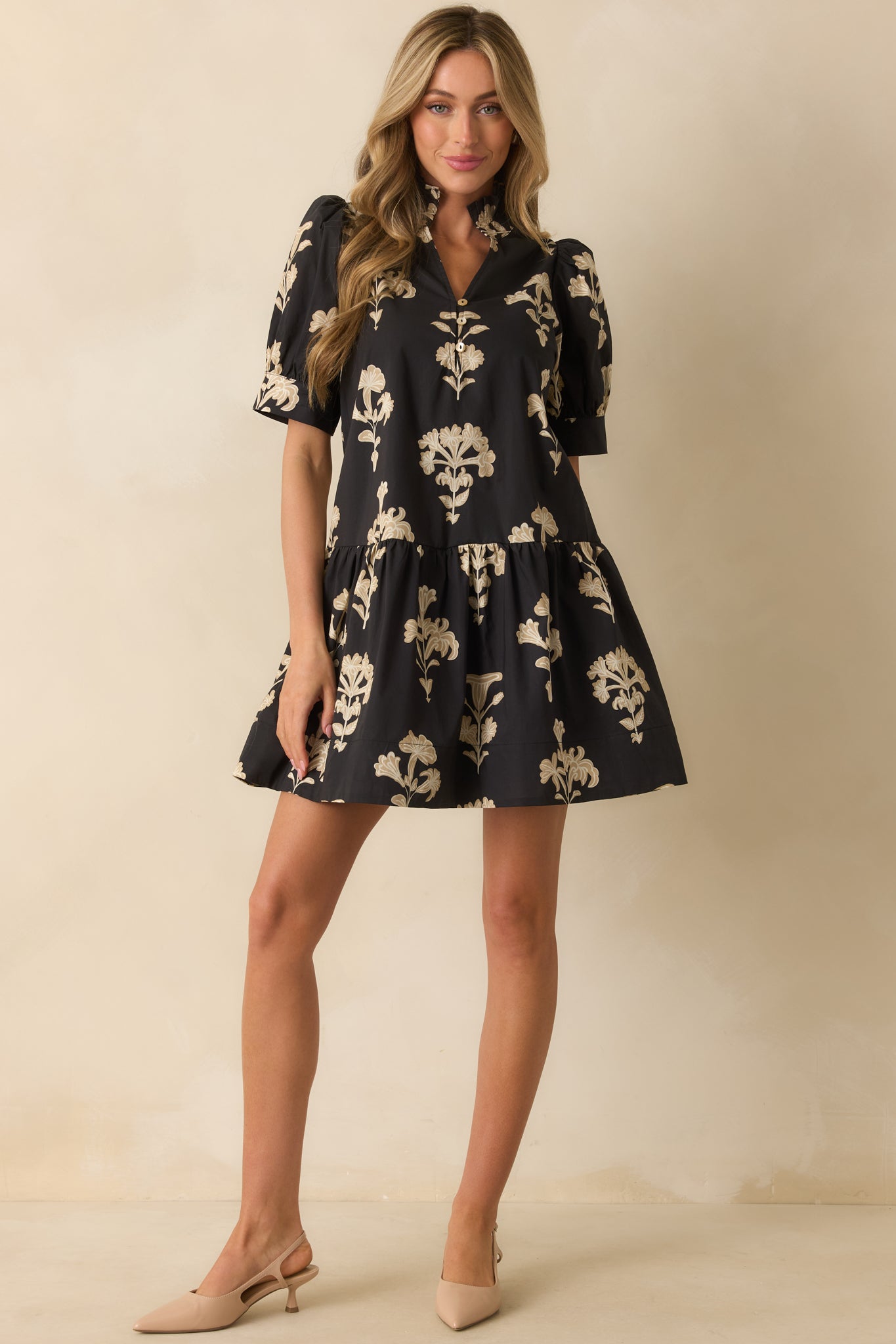Black mini dress with beige floral print, split v-neckline, short puff sleeves with cuffed hems, and a tiered babydoll silhouette.