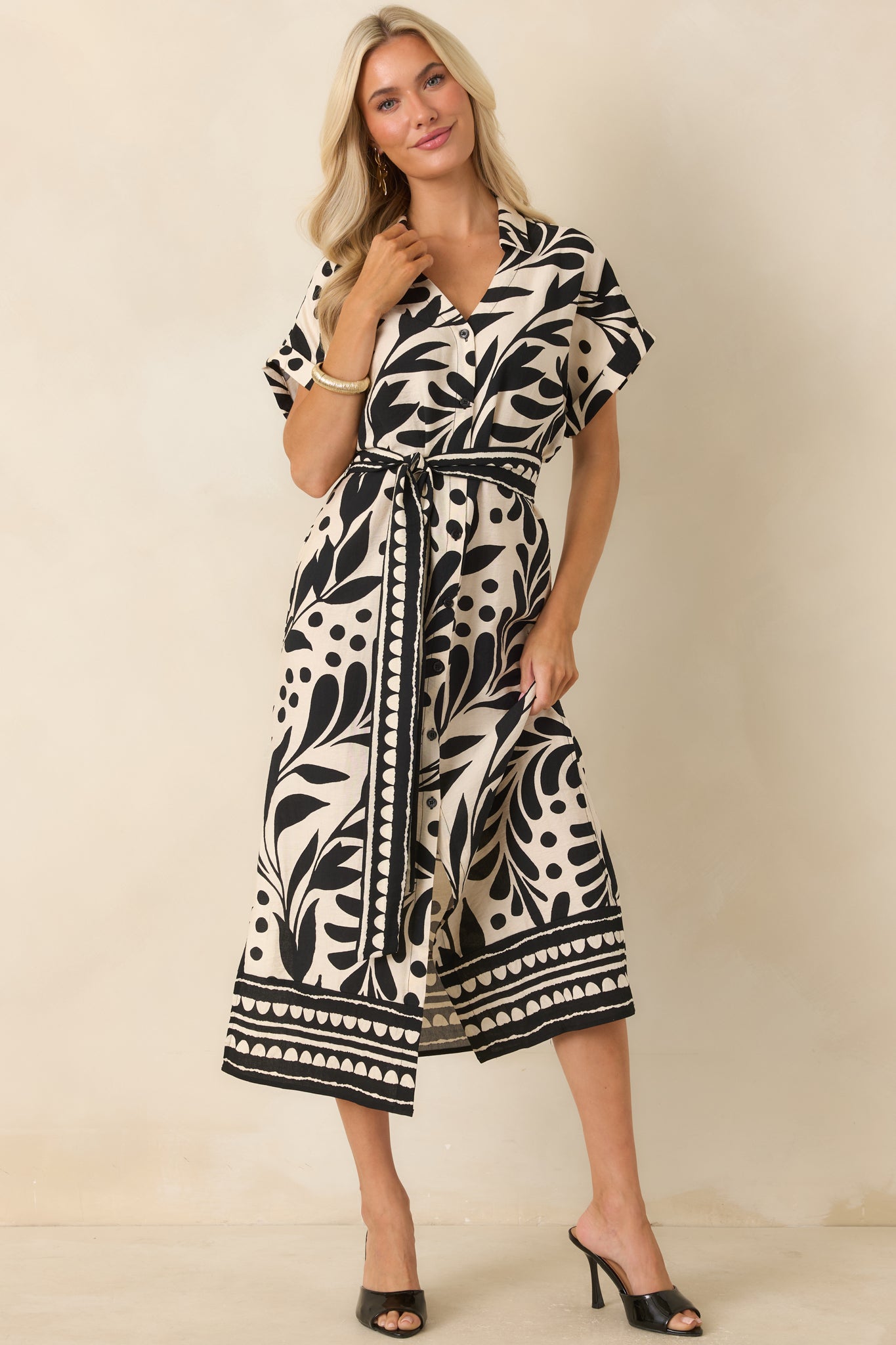 Black and natural botanical print midi dress featuring a collared neckline, button-front design, dolman sleeves, and removable waist tie.
