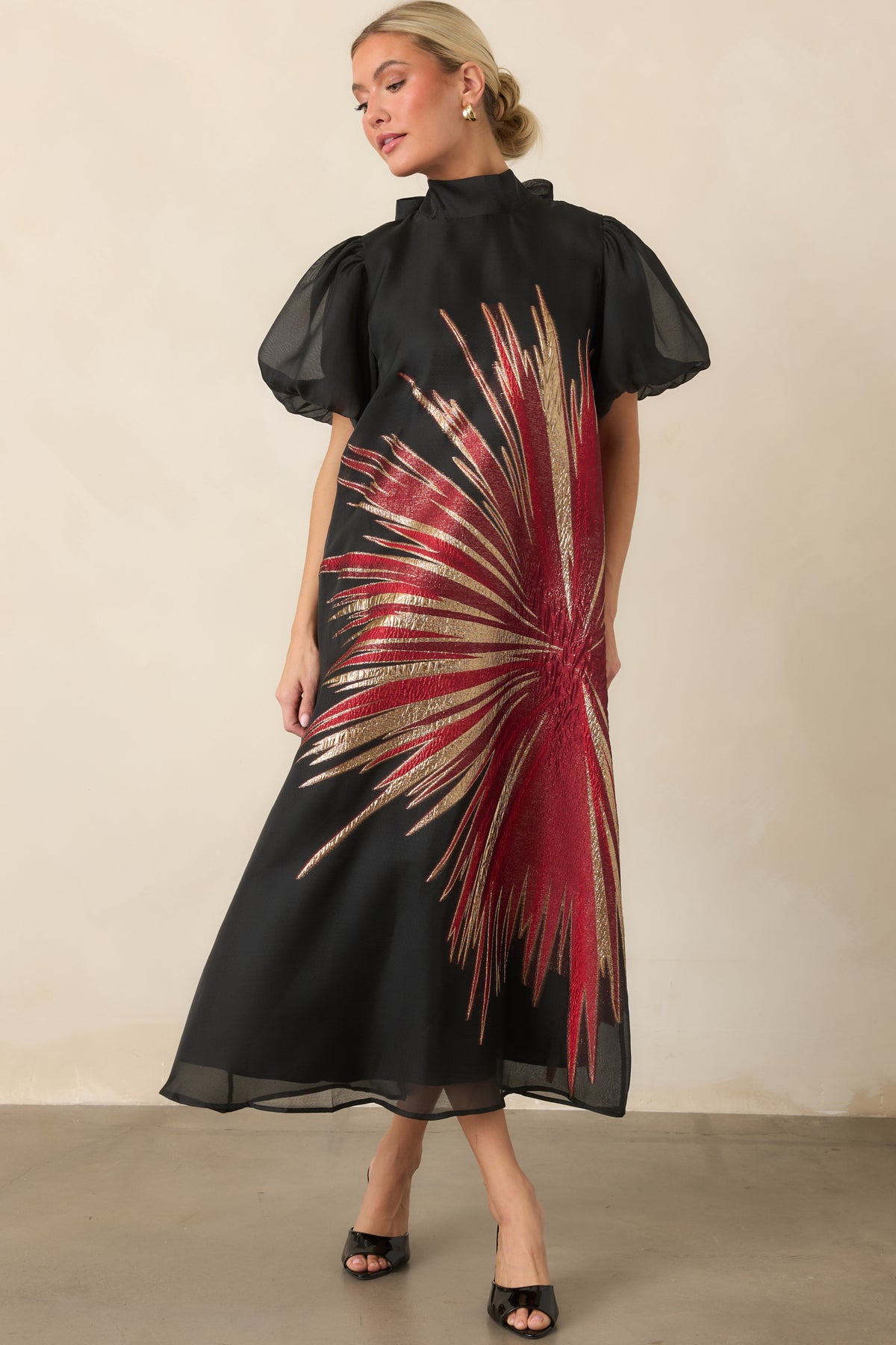 Dramatic black overlay dress showcasing the artful red and gold metallic design, high neckline, and full midi-length skirt.