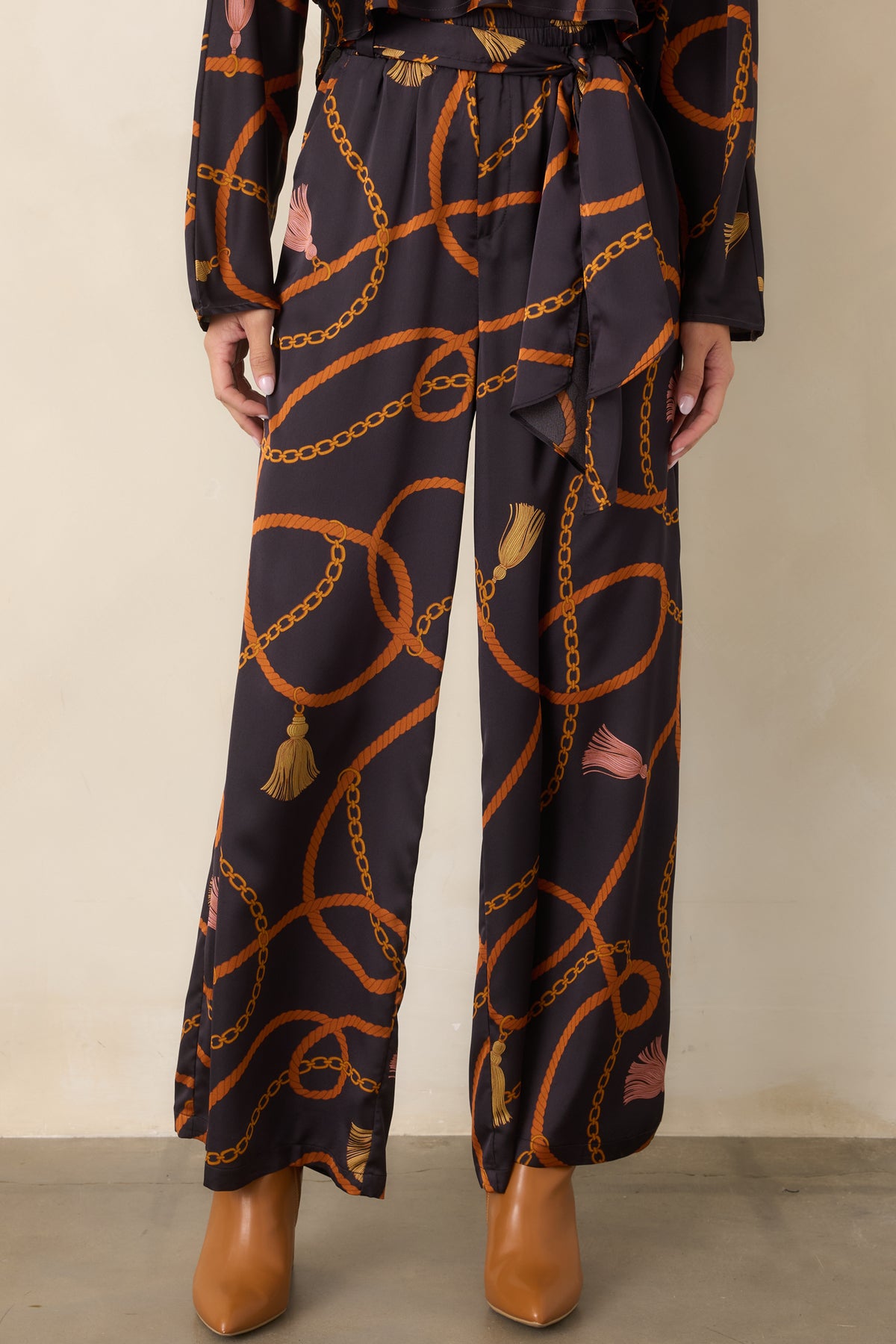 Black wide-leg pants highlighting the coordinating scarf-tie belt and intricate rust, gold, and blush chain print.