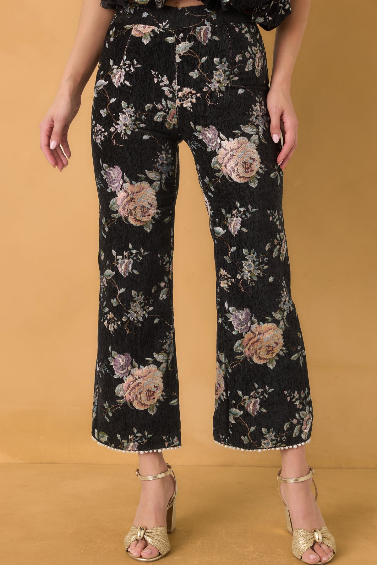 Black floral pants with muted pastel blooms, a fitted hip and thigh silhouette, and flared cropped legs.