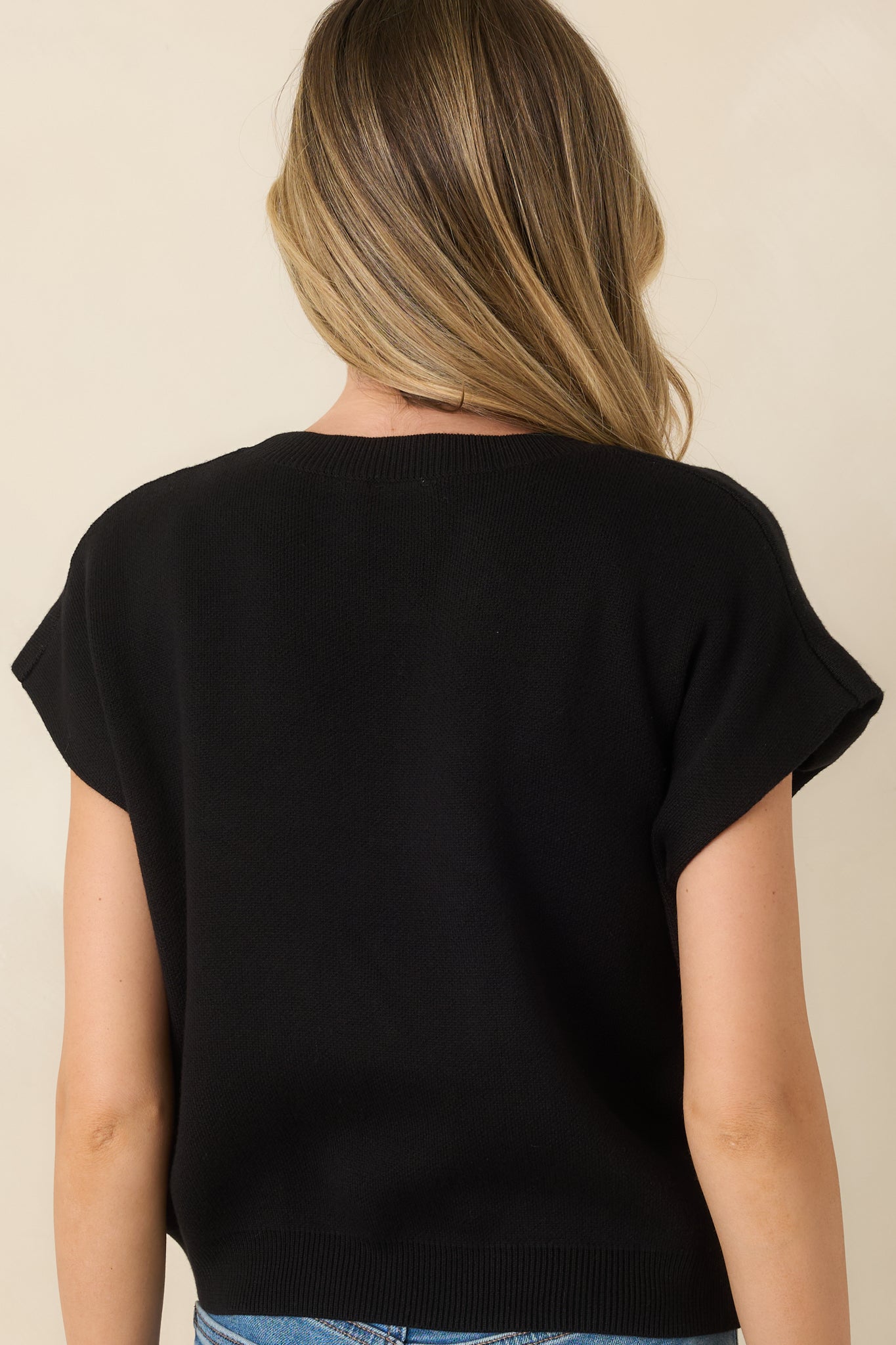 Rear view of the black knit sweater featuring a smooth, relaxed silhouette and classic cap sleeves.
