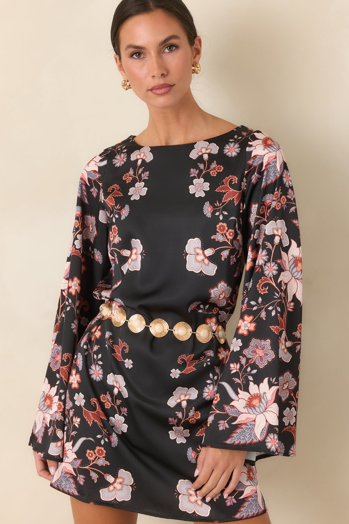 Colorful floral blooms decorate the black satin mini dress with its wide neckline and flowing sleeves.