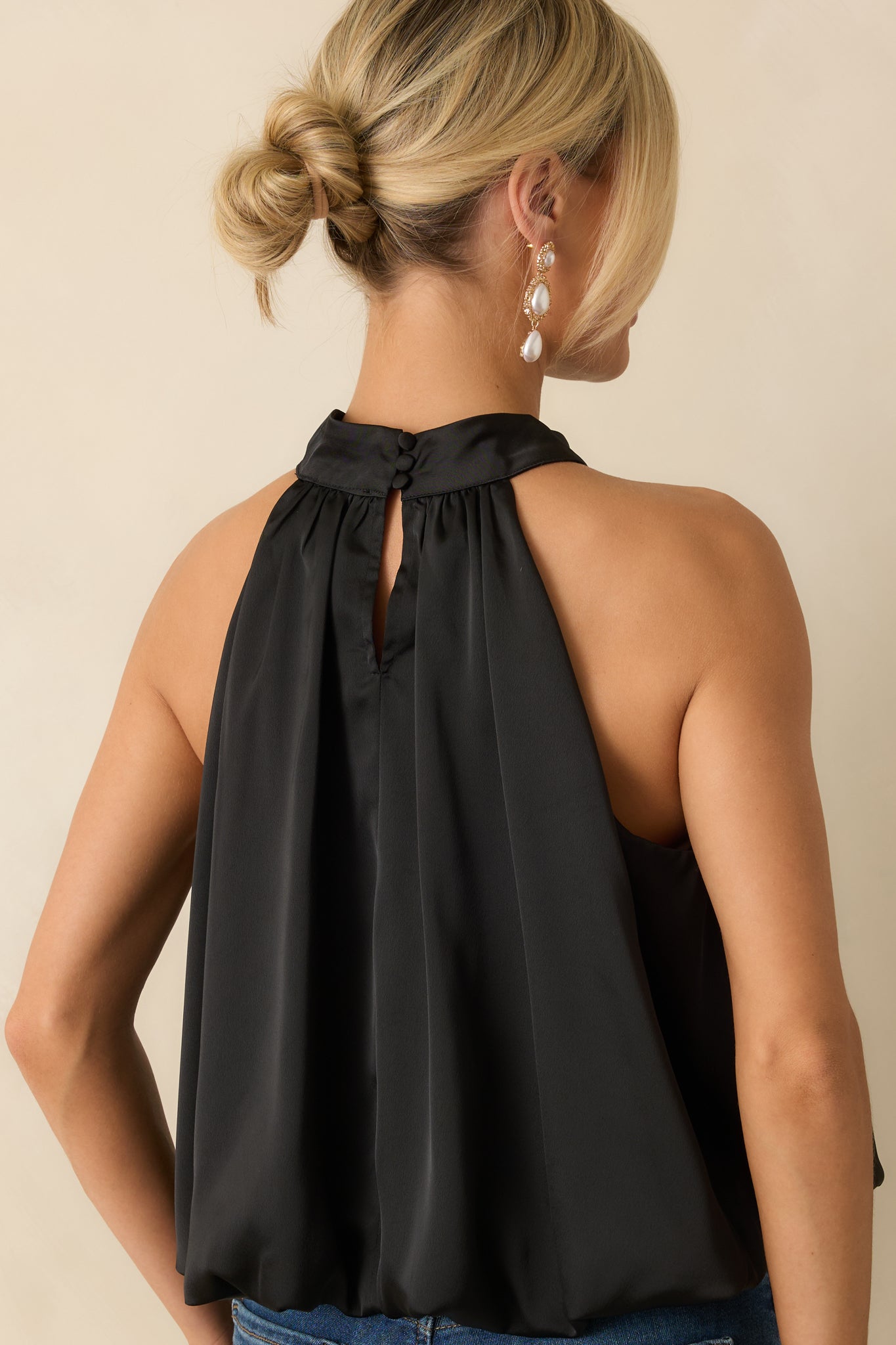 Rear view of the black satin halter top showing the button closures and softly draped silhouette.
