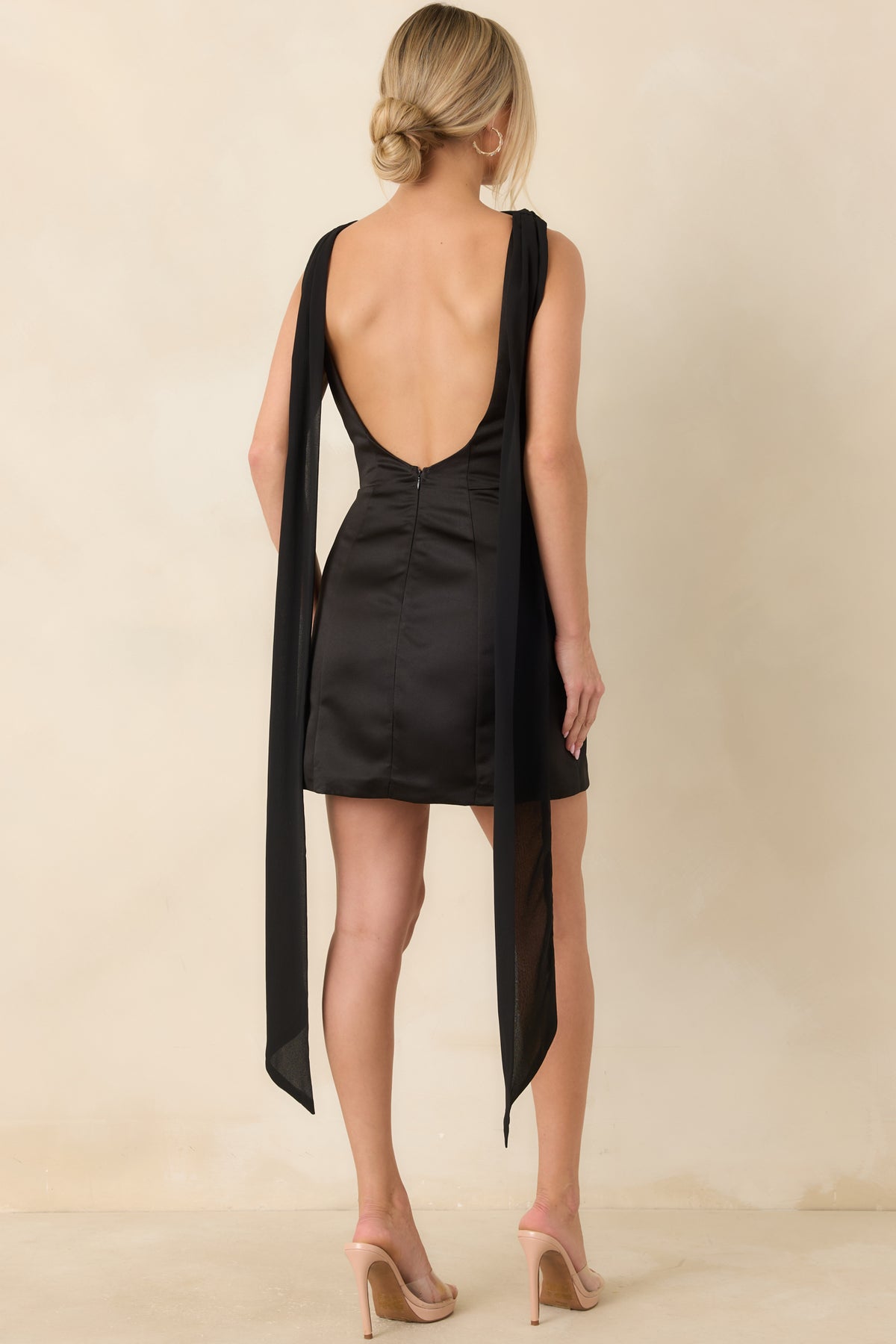 Rear view of the black satin mini dress showing the low open back and long sheer scarf panels cascading down the back.
