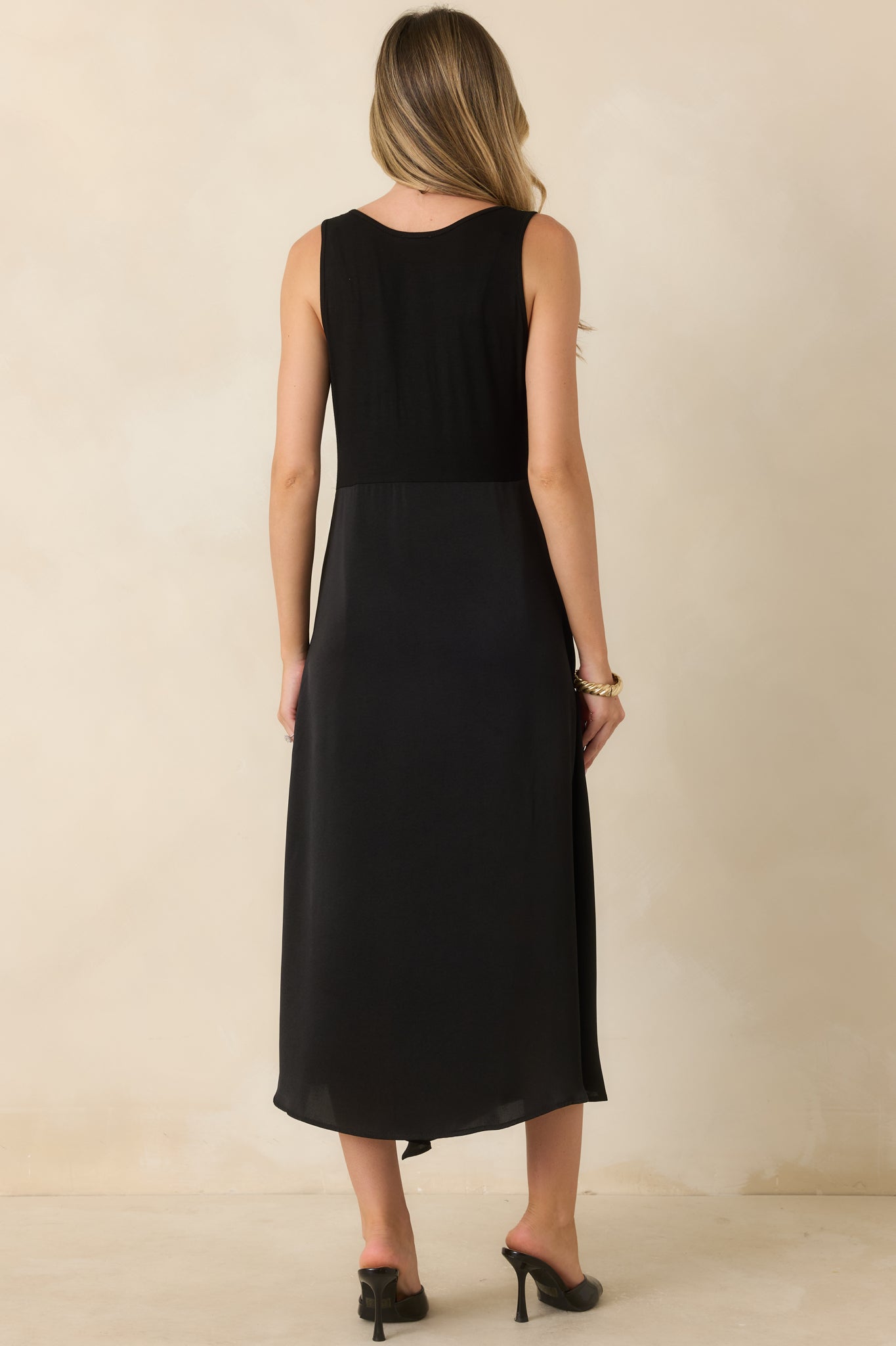 Rear view of the black sleeveless midi dress featuring a smooth knit bodice and an elegantly flowing satin skirt.