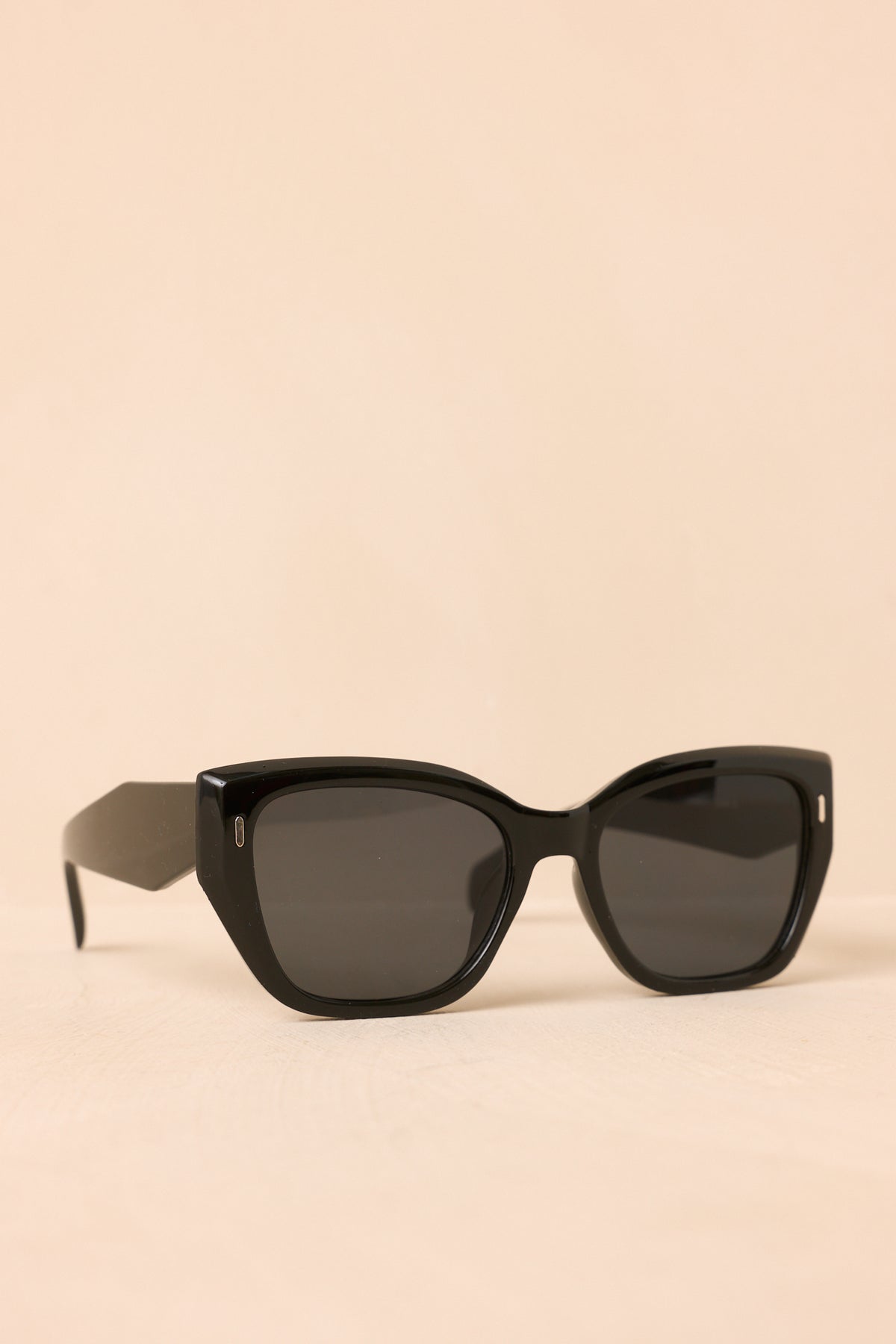 Angled black sunglasses highlight the thick temples, reflective frame finish, and small gold-tone accents near the hinges.