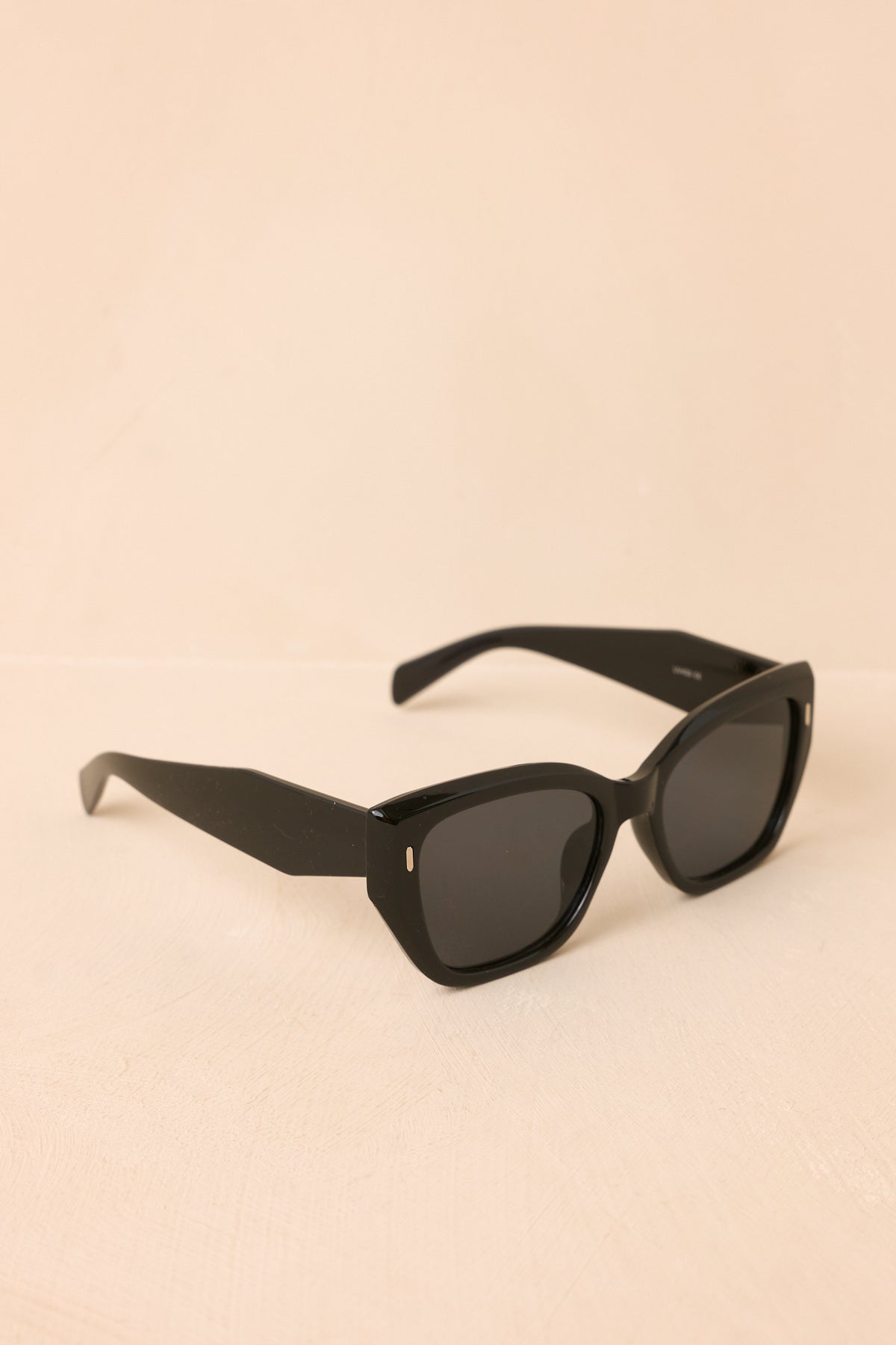 Glossy black square sunglasses feature dark lenses, wide arms, and subtle gold-tone accents along the temples.
