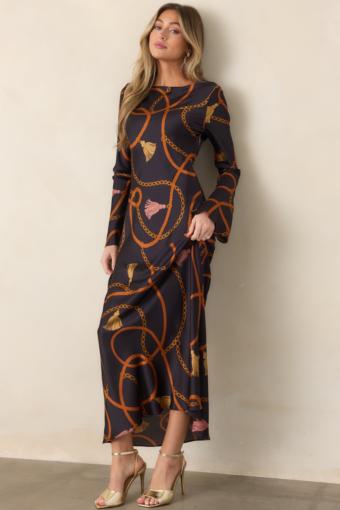 Statement black maxi dress showcasing the fluid satin fabric and richly detailed rust, gold, and tassel pattern.