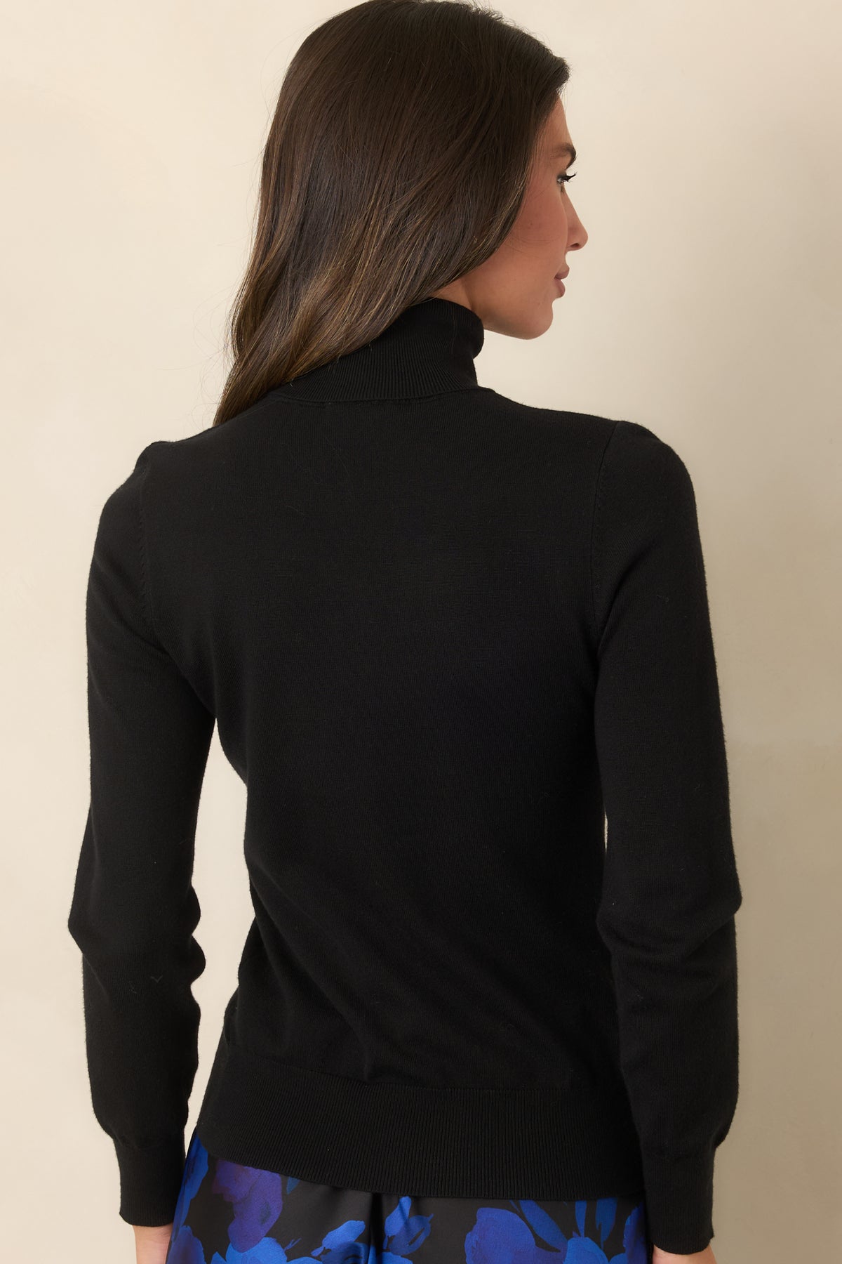 Rear of the black sweater showing the ribbed hem and long sleeves.