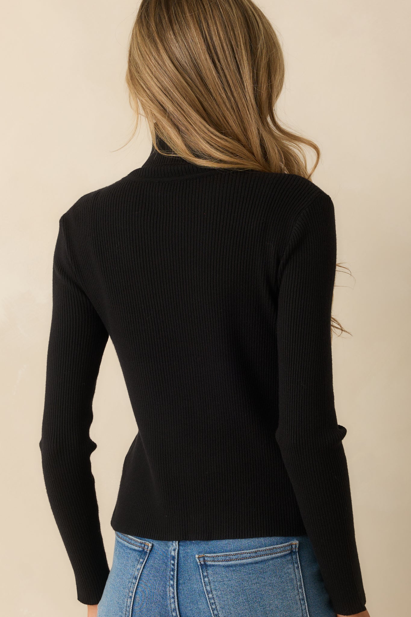 Rear view showing the fitted shape, long sleeves, and ribbed texture of the black sweater.