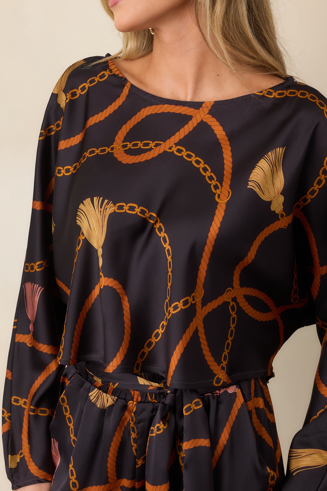 Close-up of the satin-feel fabric displaying looping rust ropes, golden chains, and tassel accents against black.