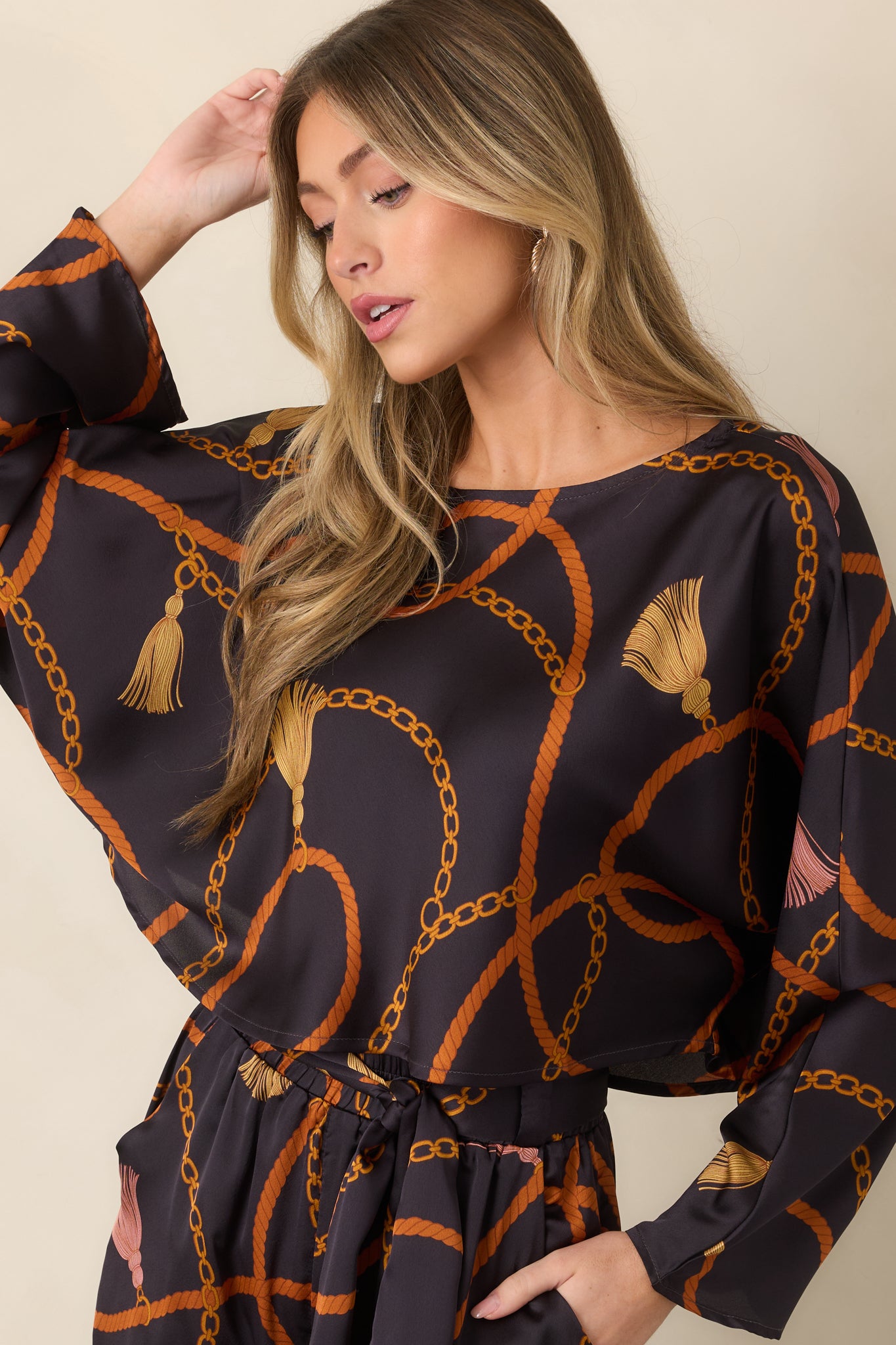 Close view of the black top’s round neckline and silky fabric adorned with rust rope and gold chain motifs.