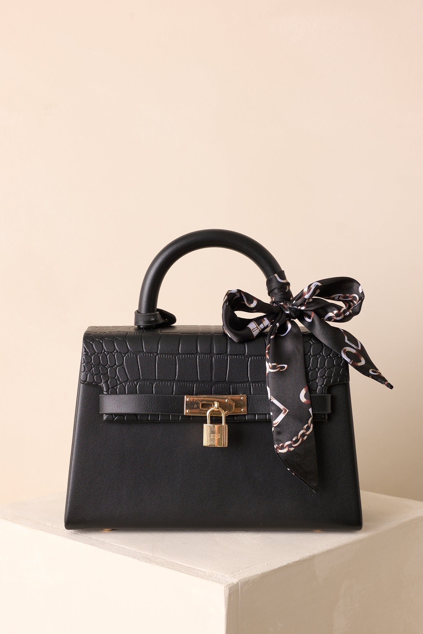 A cropped front view of the black handbag highlighting the padlock closure and croc texture of the flap.