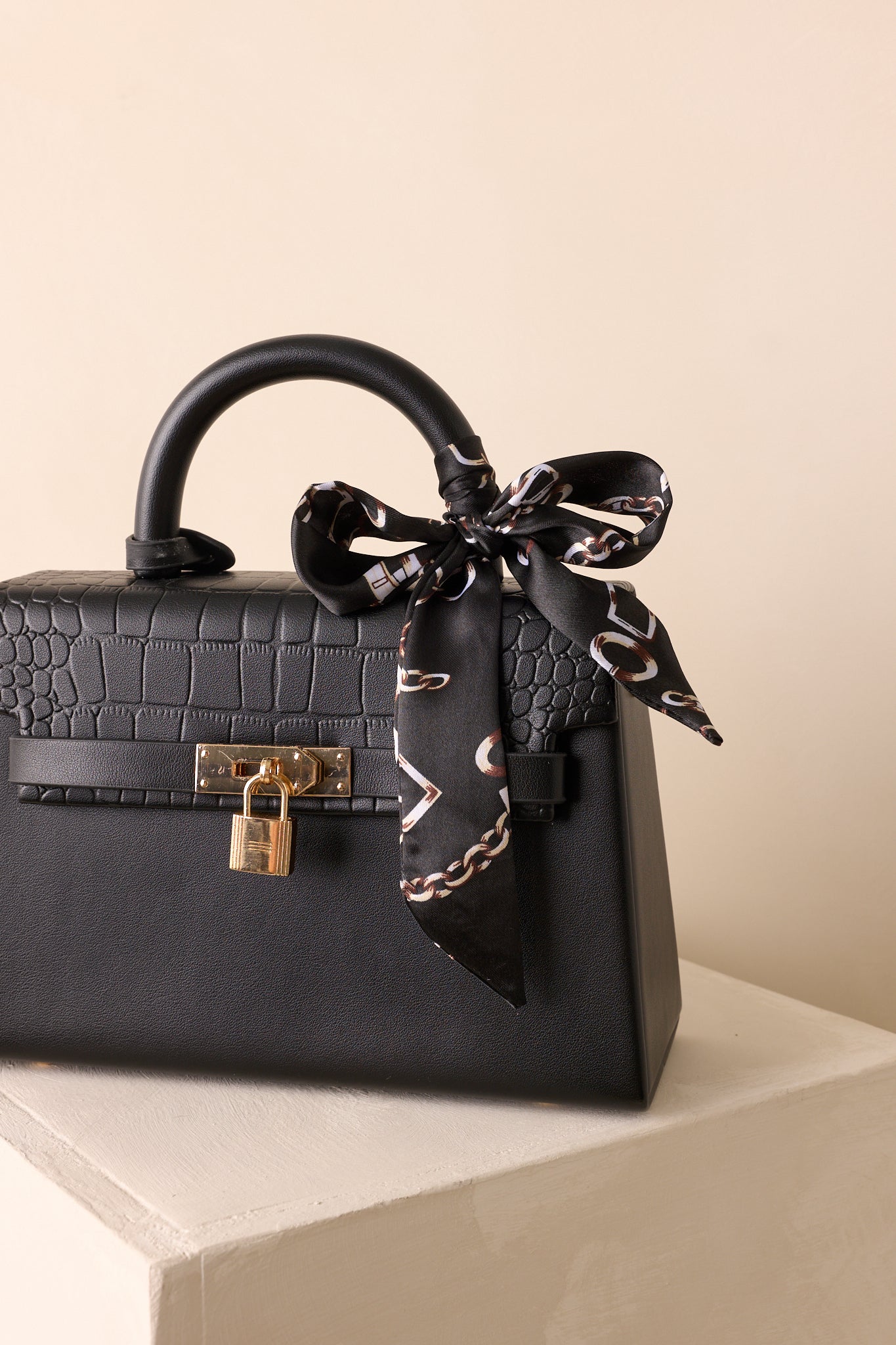 Detailed close-up of black handbag showing padlock closure, magnetic flap, and texture of faux leather.