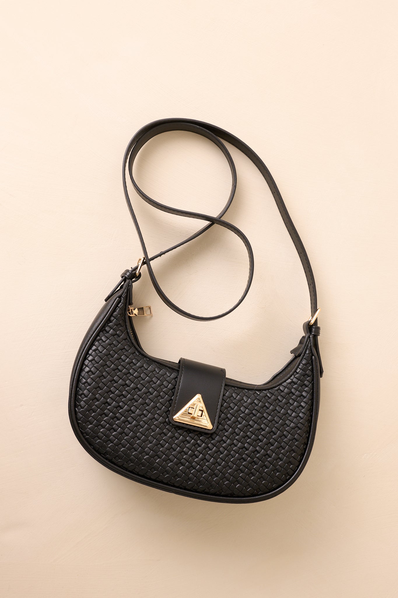 Front-facing full view of the black shoulder bag showing the curved half-moon shape, woven faux leather texture, and gold triangular twist-lock flap closure.
