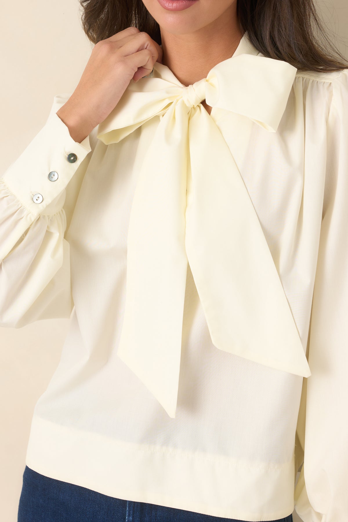 Close-up highlights the statement neckline tie, gathered shoulder seams, and wide button cuff detailing.