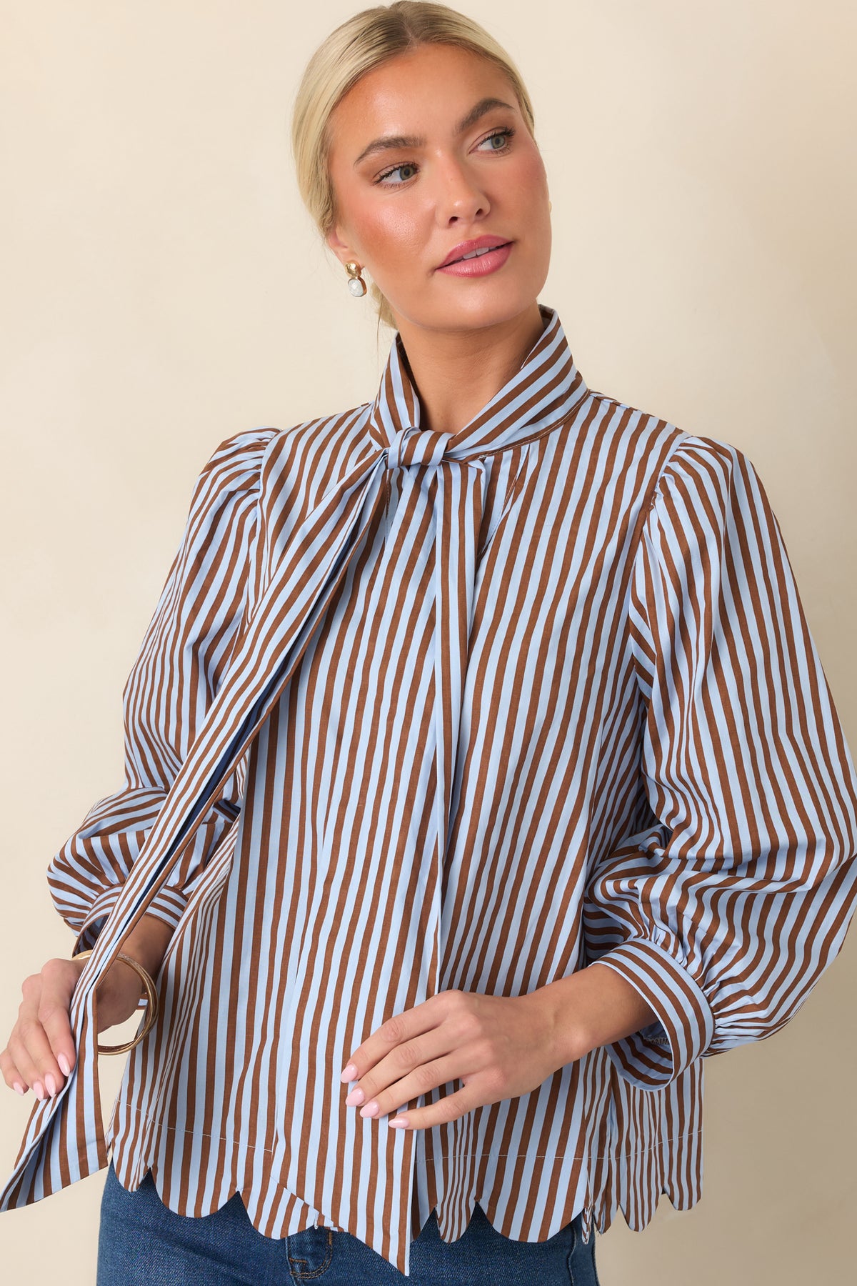 Blue and brown striped blouse displaying its softly gathered shoulders, tied neckline, and feminine silhouette.