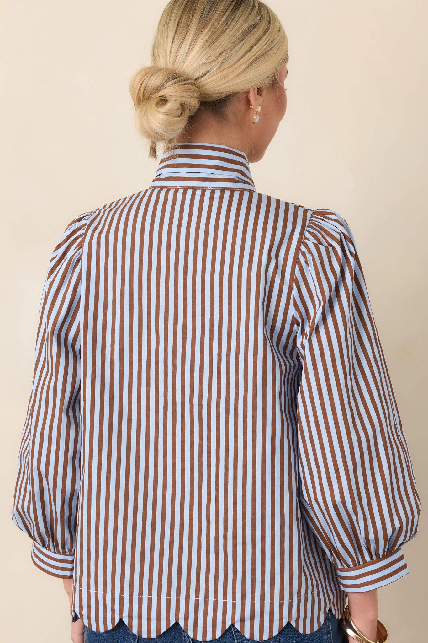 Rear view of the blue and brown striped blouse showcasing its gathered shoulders, voluminous sleeves, and scalloped hem.
