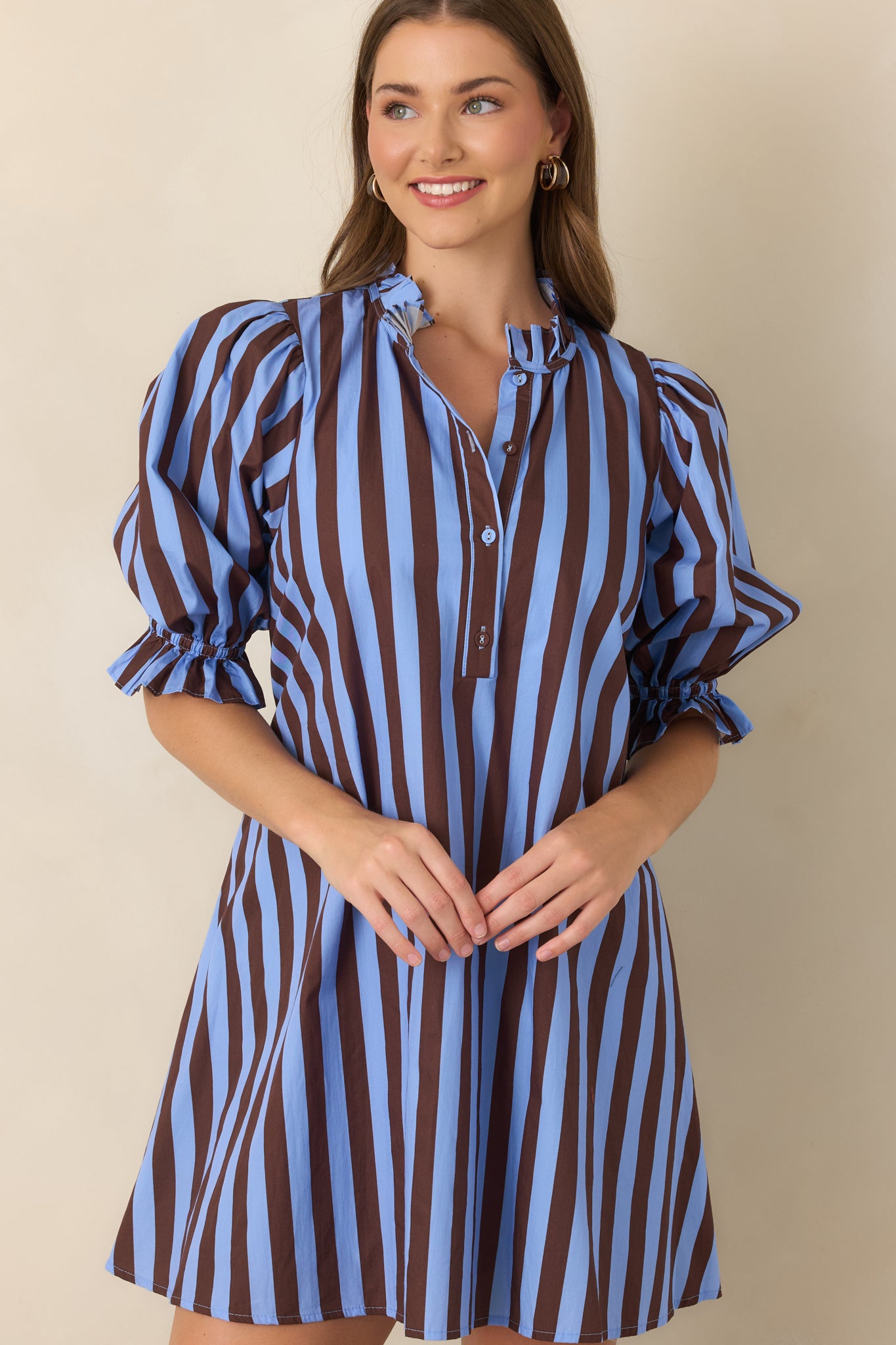 Blue and brown striped dress showcasing the feminine ruffle detailing along the mock collar and cuffs with a partially buttoned front.